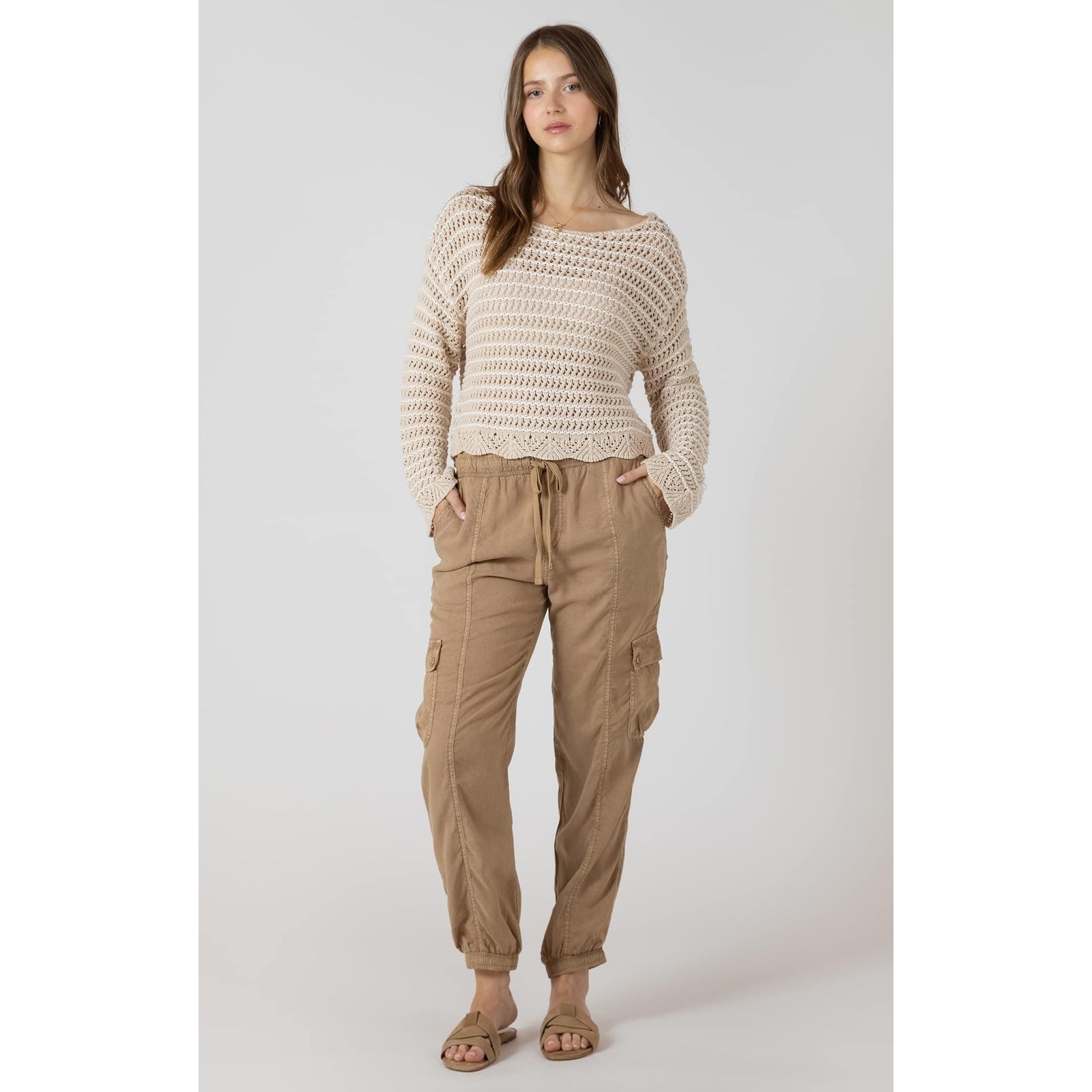 Model wearing cream Dex Open Stitch Scalloped Hem Sweater, open-knit with scalloped hem, paired with tan cargo pants.