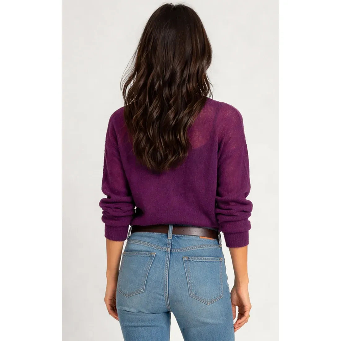 Back view of a woman wearing a purple sheer sweater top with rolled sleeves, styled with blue jeans and a brown belt.