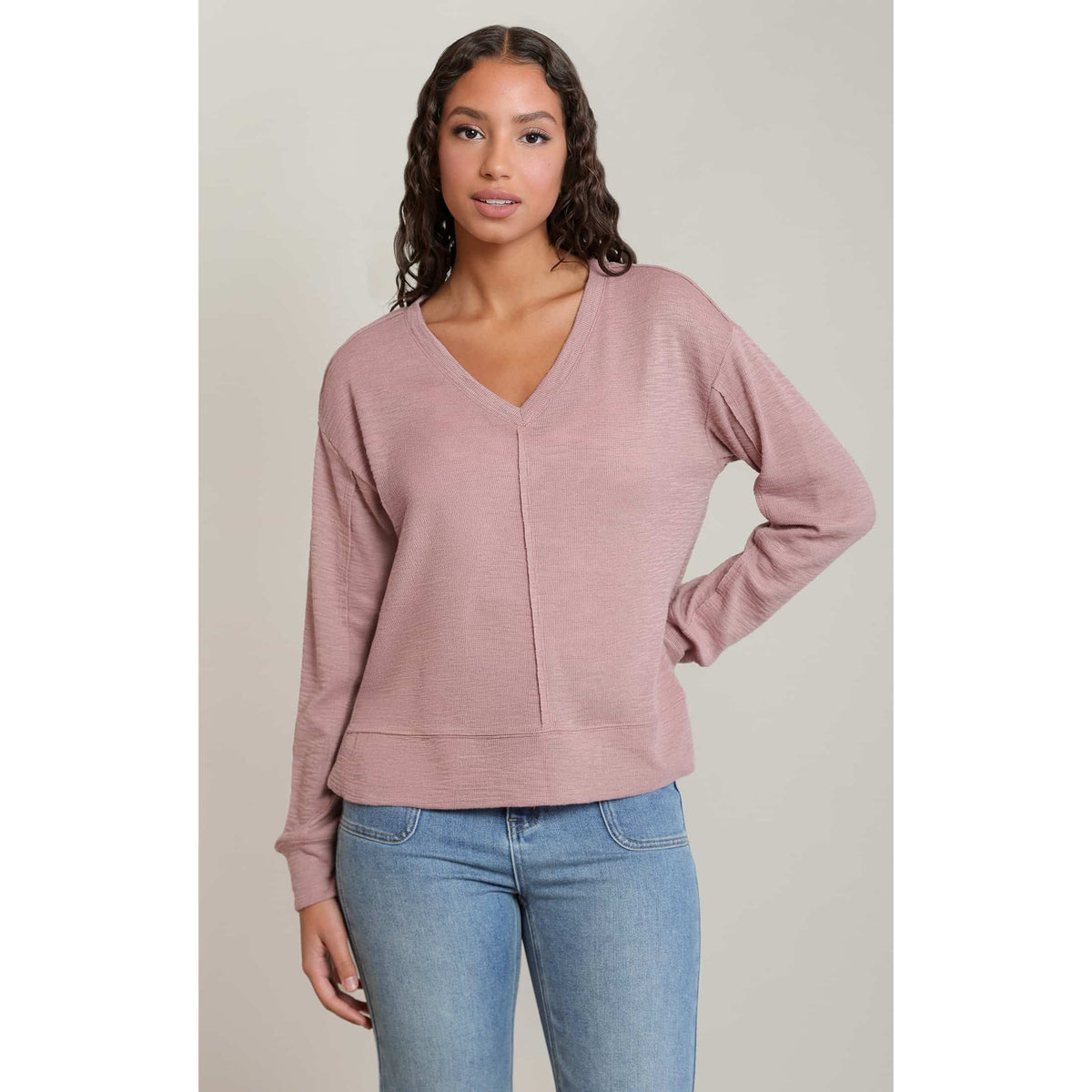 Dusty pink Dex V-Neck long-sleeve knit top with raw seams and relaxed fit, styled with denim.