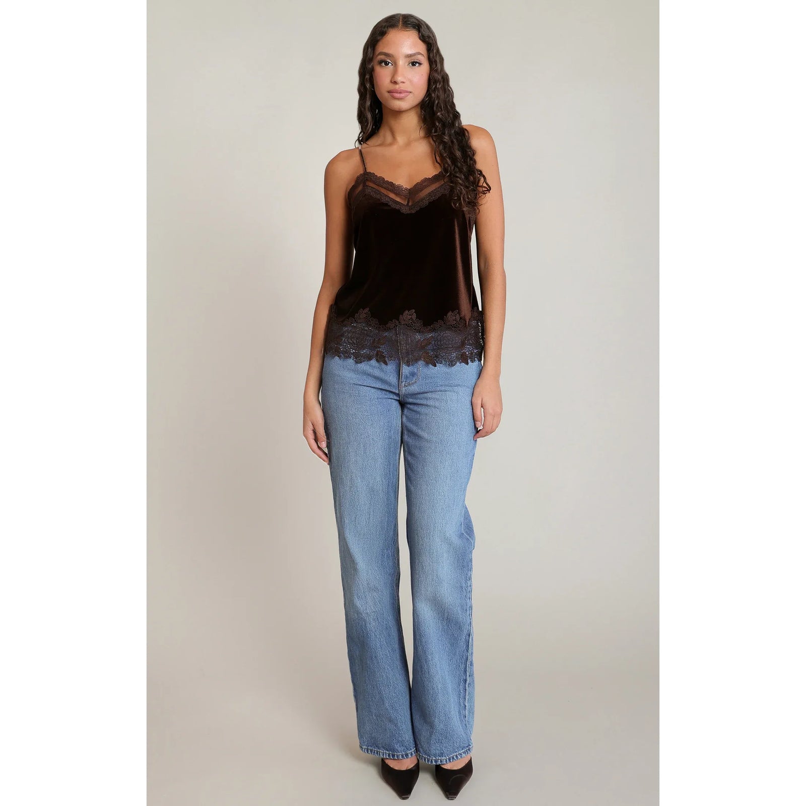Model wearing a chocolate brown velvet lace cami with spaghetti straps and floral lace trim at the neckline and hem, styled with blue jeans.