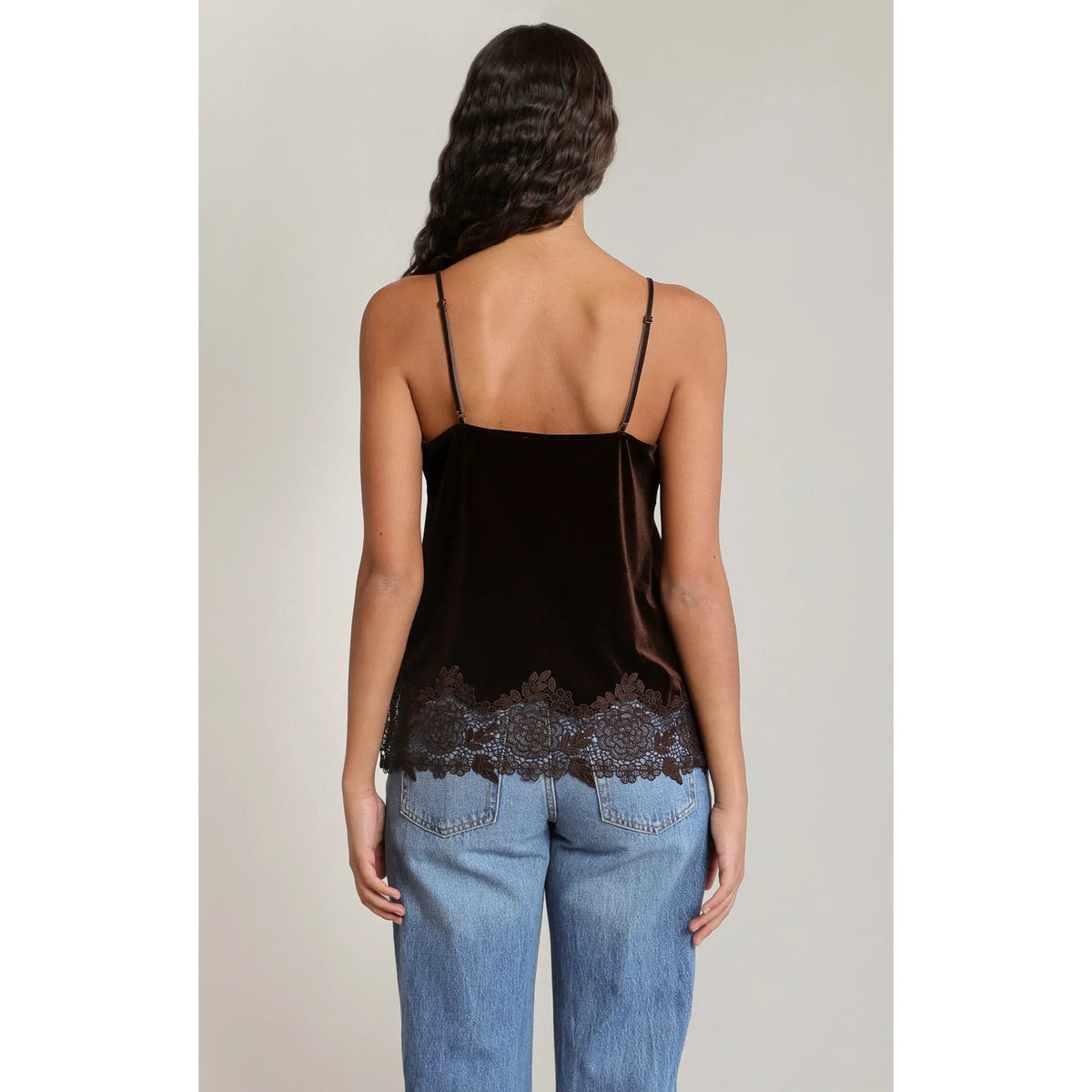 Back view of a chocolate brown velvet lace cami with adjustable spaghetti straps and floral lace trim hem worn with denim jeans.