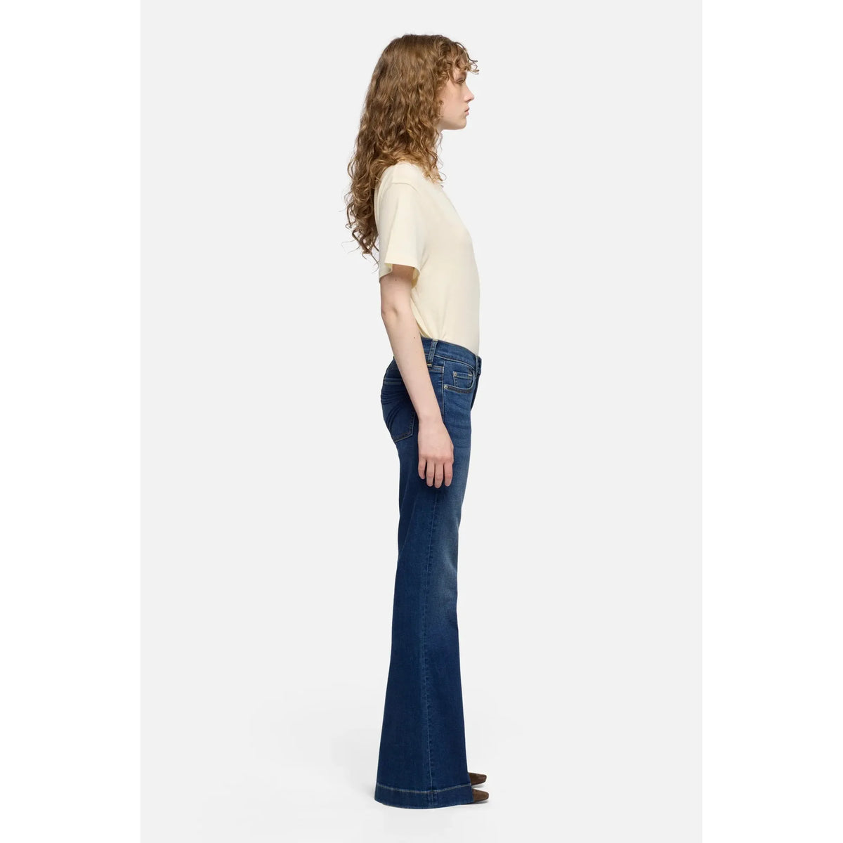 Side view of a woman wearing 7 For All Mankind Dojo Melrose mid-rise flare jeans with a cream T-shirt.