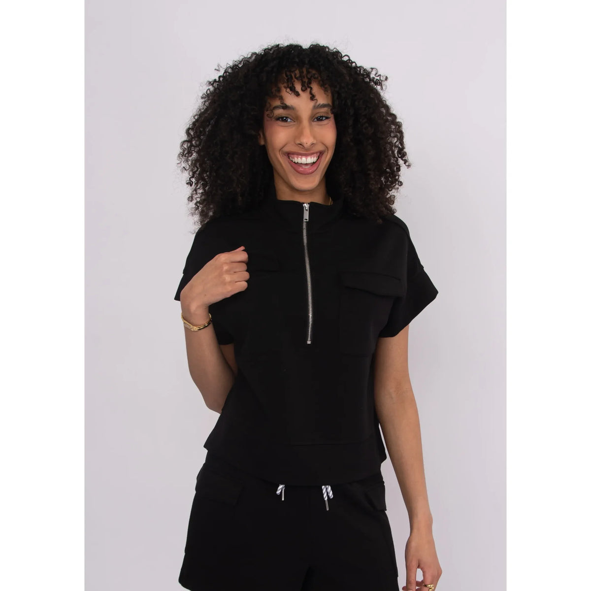 Smiling model wearing Dua Soft Knit 1/2 Zip Top in black with short sleeves, front zip and chest pockets.