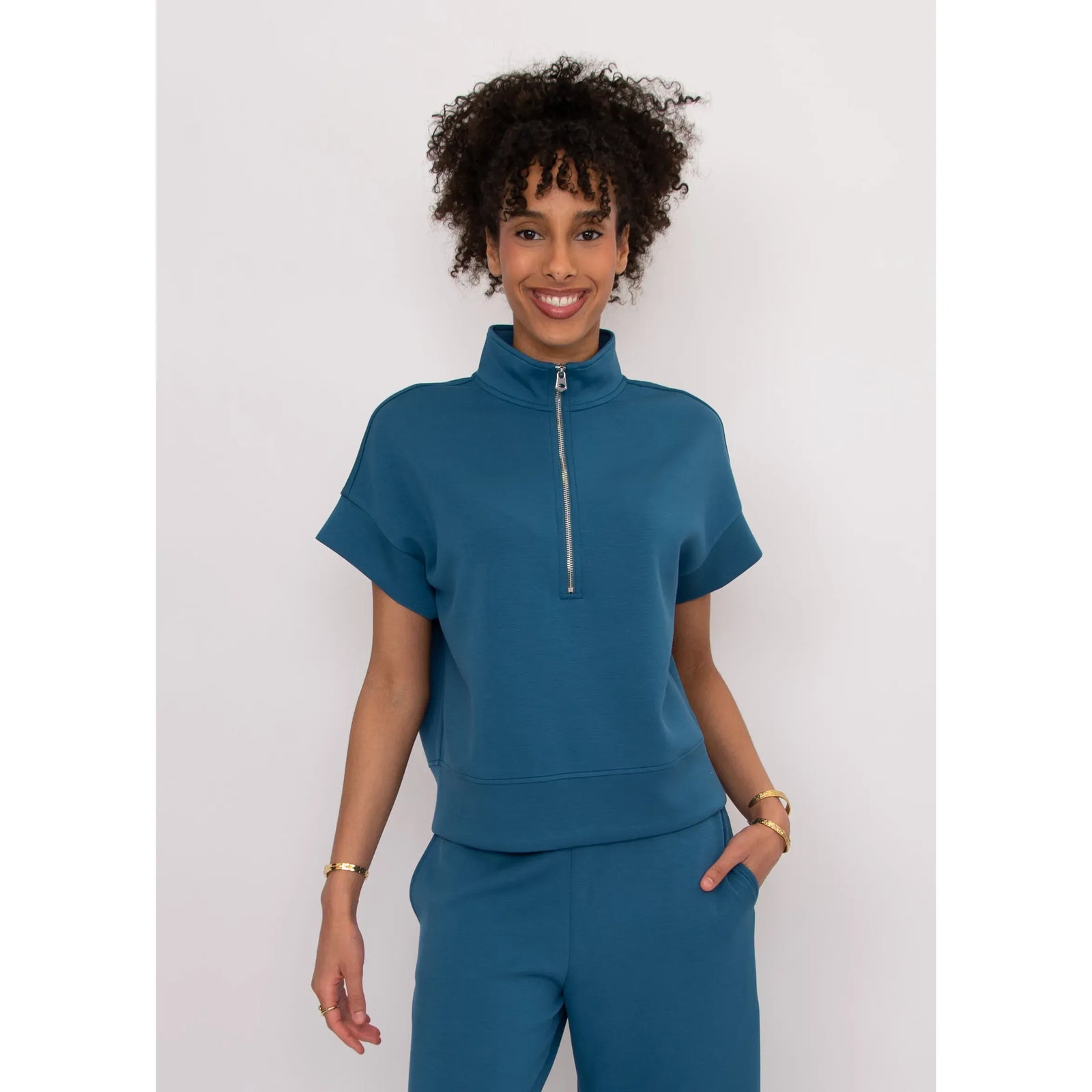 Dua Soft Knit 1/2 Zip Top in teal blue with short cuffed sleeves and front zipper on a smiling model.