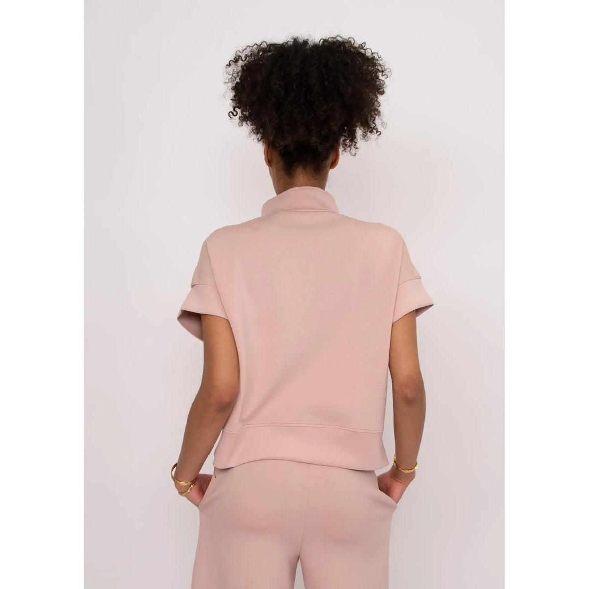 Back view of a model in a pink Dua Soft Knit 1/2 Zip Top with short cuffed sleeves.