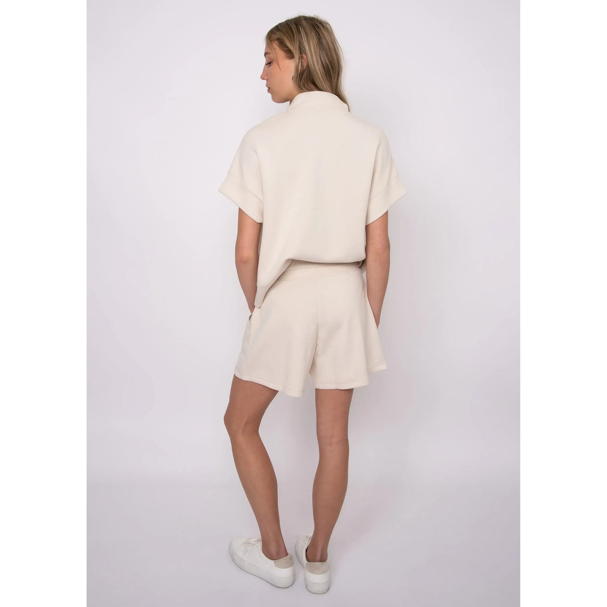 Back view of a model wearing the Dua Soft Knit 1/2 Zip Top in cream with short cuffed sleeves.