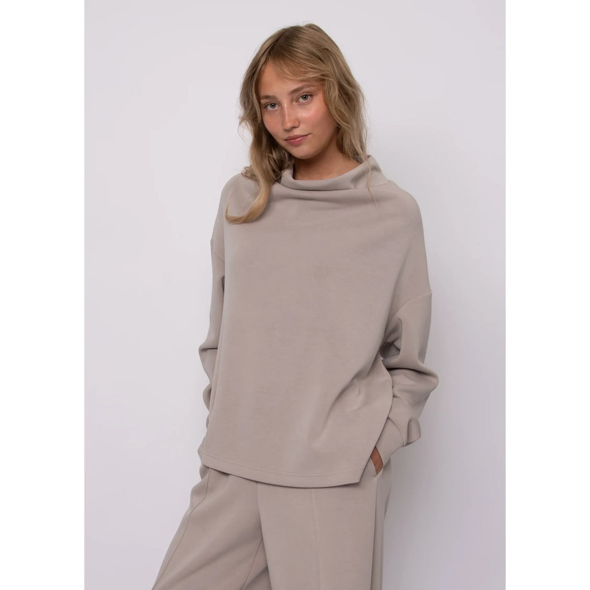 Model wearing a beige soft knit funnel neck top with long sleeves and a cozy stand-up neckline for everyday style.