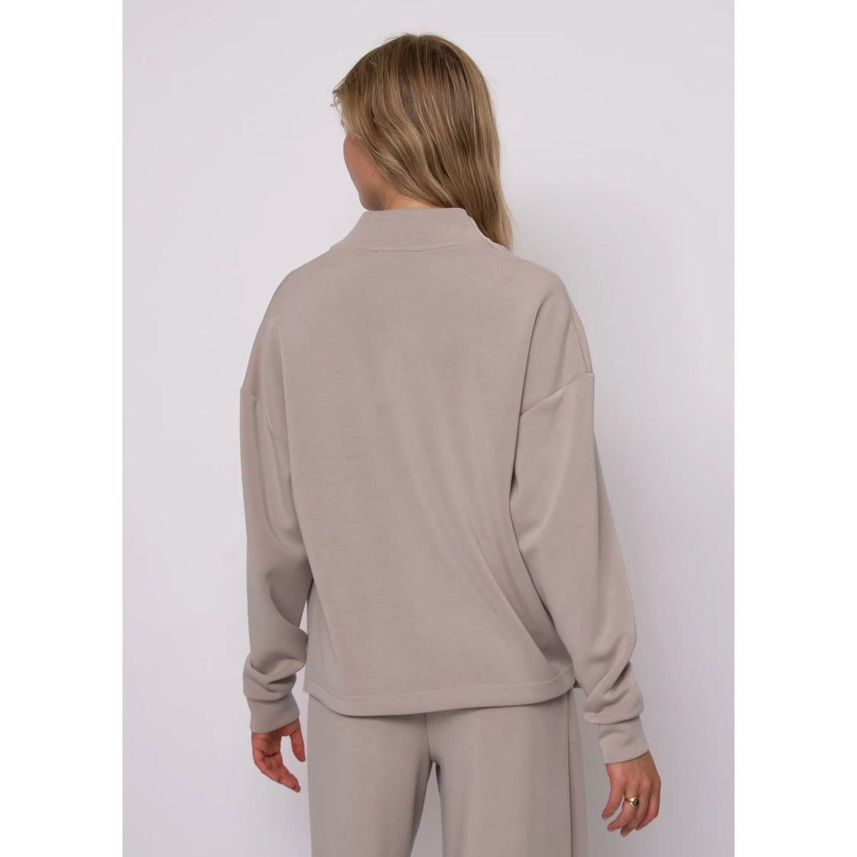Back view of a beige soft knit funnel neck top with long sleeves, offering refined warmth and effortless everyday style.