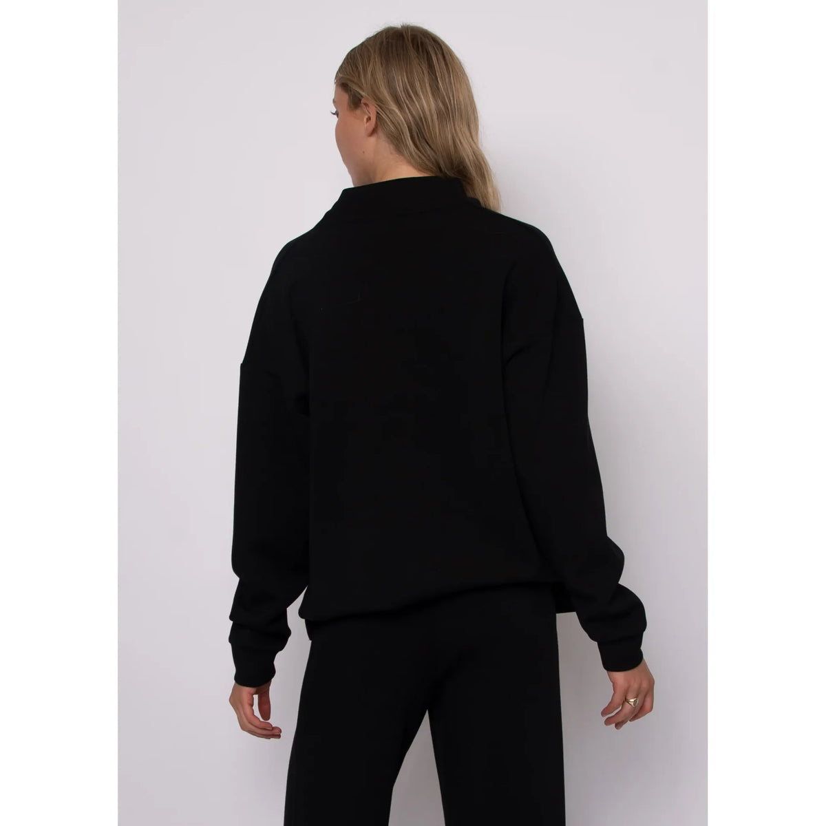 Back view of a black soft knit funnel neck top with long sleeves and a cozy stand-up collar.