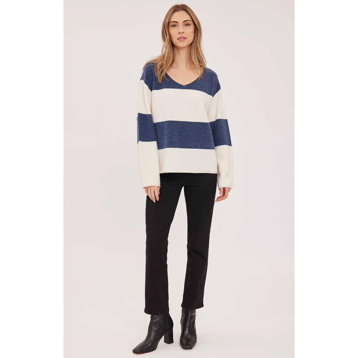 Oversized V-neck sweater in blue and cream stripes with soft textured knit, rolled edges, and relaxed fit paired with black boots.