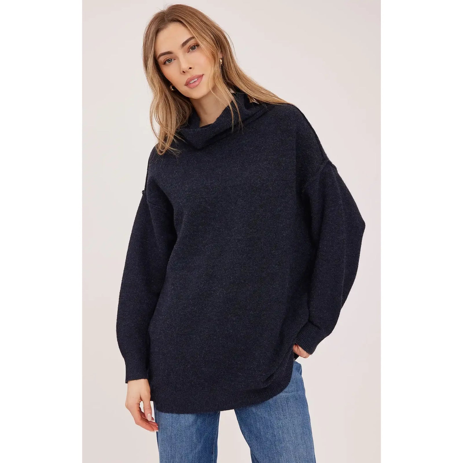 Model wearing a dark navy oversized turtleneck sweater with a textured knit and dropped shoulders paired with blue jeans.