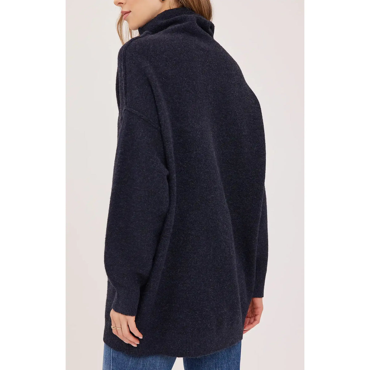 Back view of the oversized Astrid sweater featuring a slouchy turtleneck, exposed seam details, and soft textured yarn in dark charcoal.