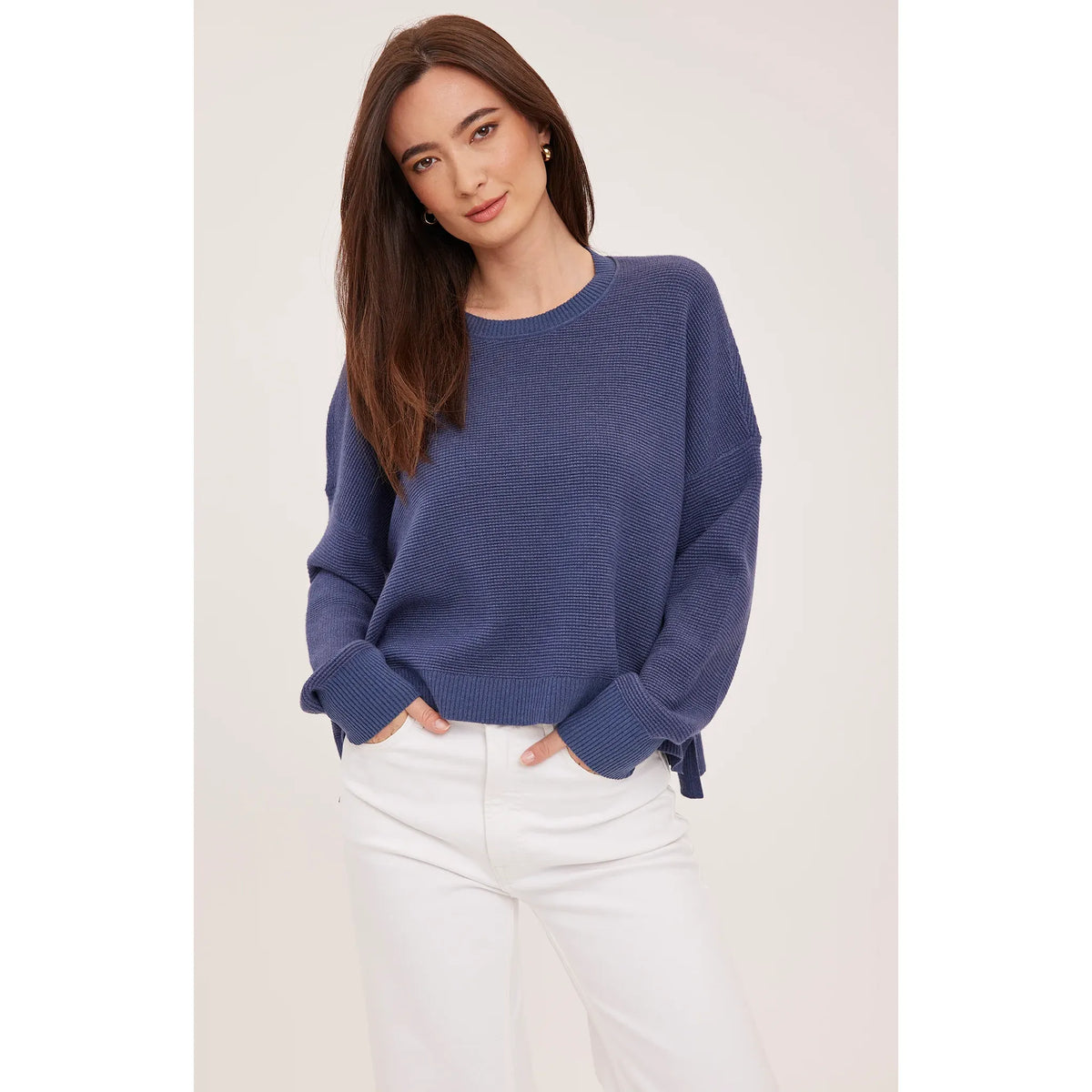 Blue waffle knit crewneck sweater with oversized fit and side slits, styled with white jeans.