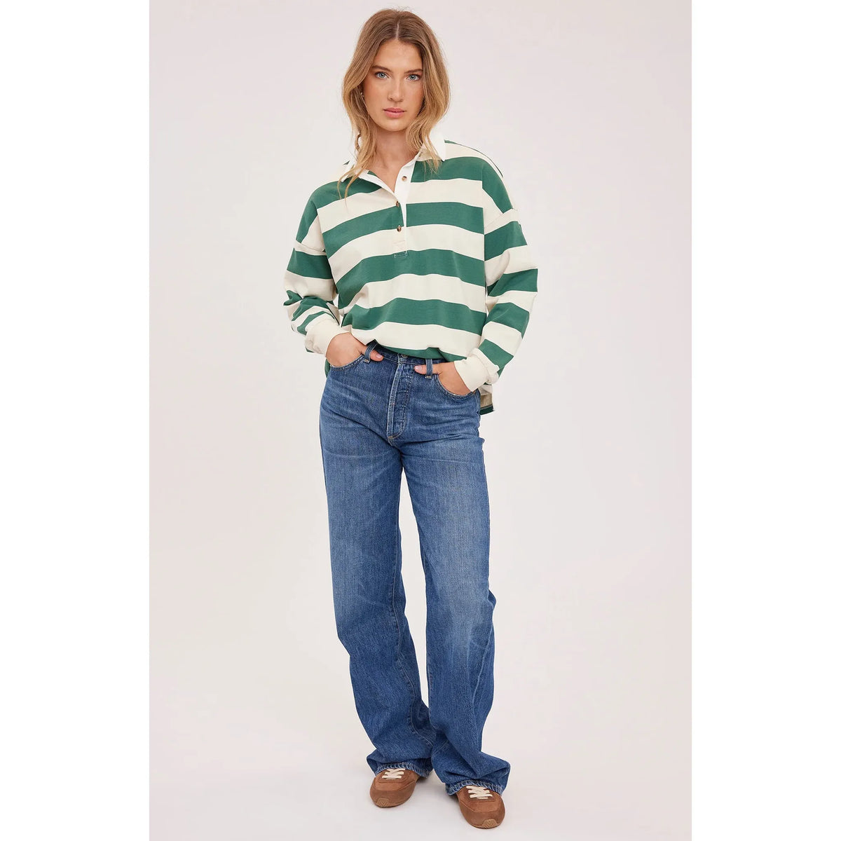 Model in green-and-white striped rugby shirt with contrasting collar and half-button placket, in blue jeans.