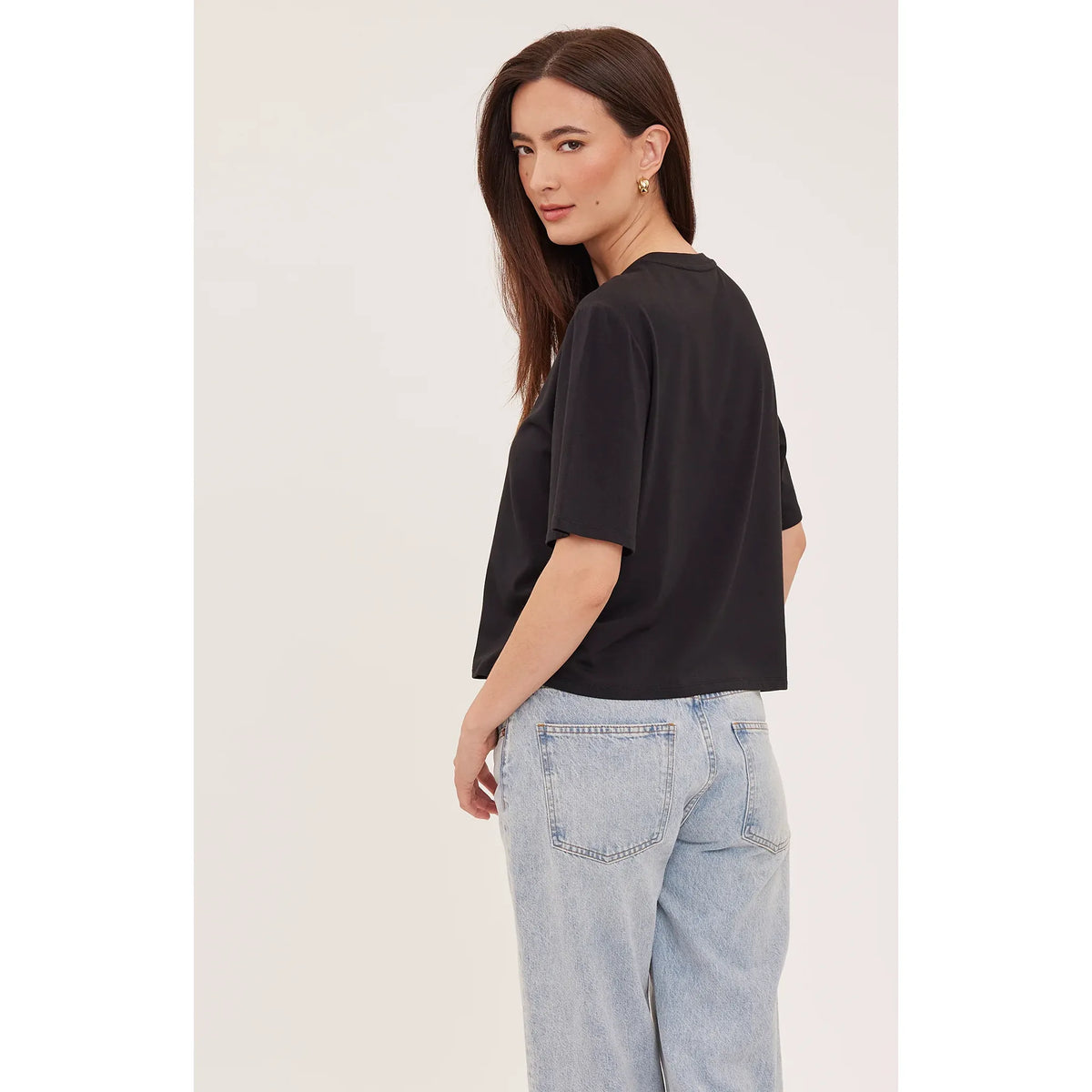 Back view of a model wearing a black relaxed fit Codie T-shirt with short sleeves and light blue jeans.