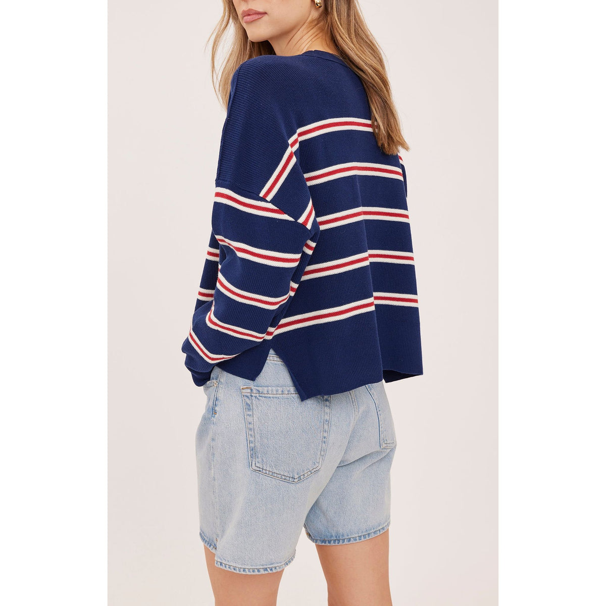 Back view of oversized navy striped sweater with red and white lines, featuring side slits and soft knit texture paired with denim shorts.