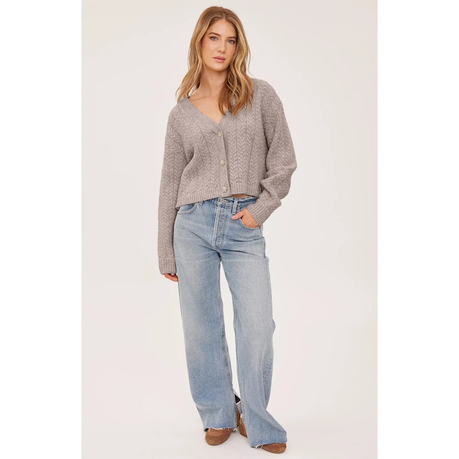 Soft fawn bouclé cable knit cardigan with a relaxed fit, V-neckline, and button-front closure paired with light wash jeans.