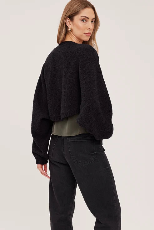 Black cropped open-front bouclé cardigan with voluminous sleeves and fitted rib cuffs, styled over an olive top and black jeans.