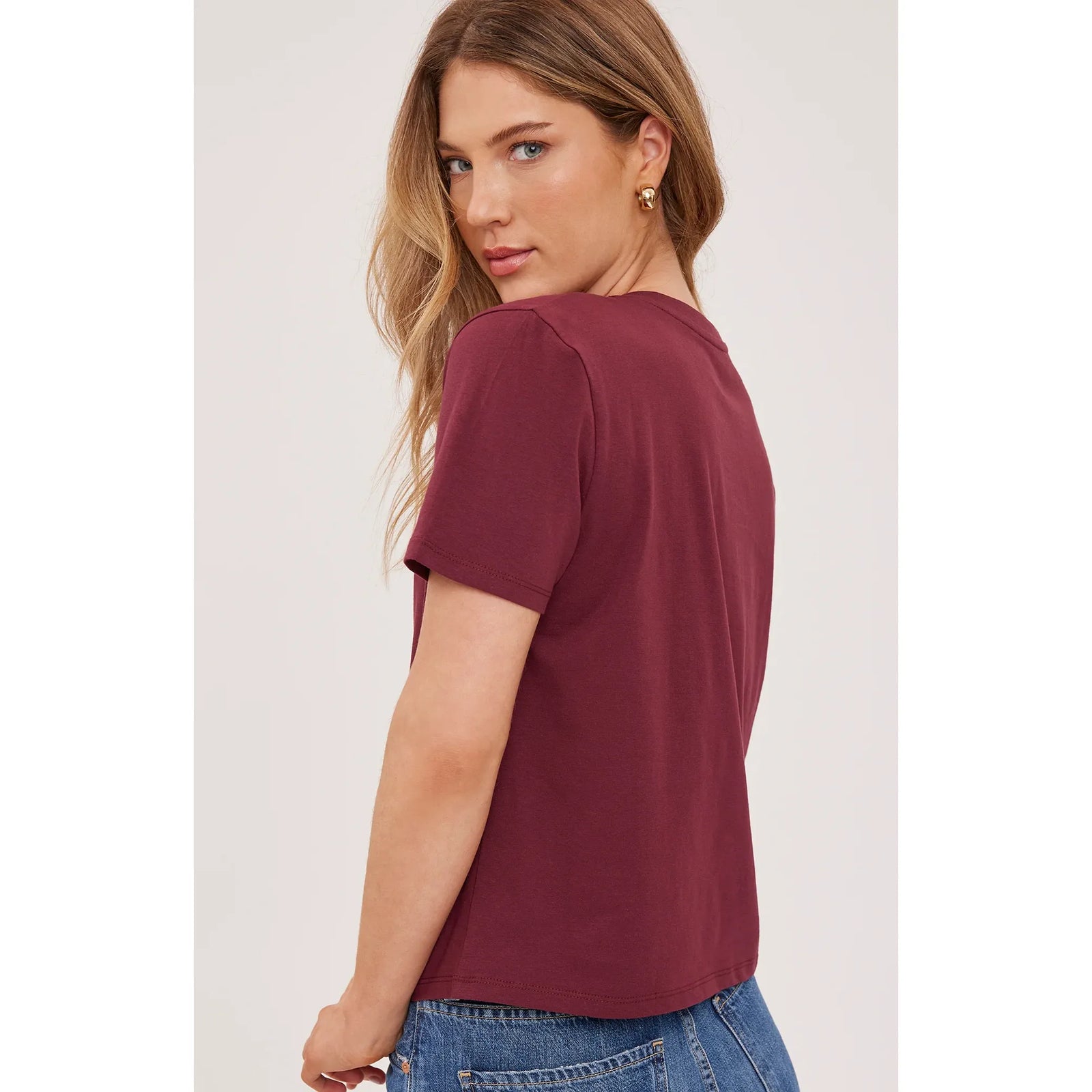 Womam wearing a maroon cropped short sleeve cotton top with a v-neck, styled with blue jeans against a white background.