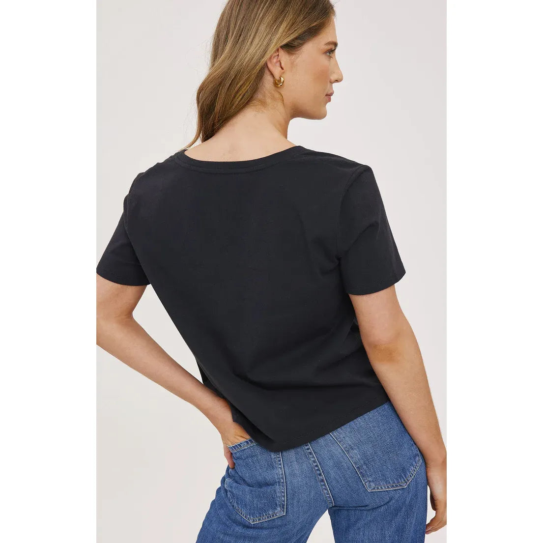 Back view of a woman wearing a black Gentle Fawn Lucy Top, cropped short-sleeve tee paired with jeans.
