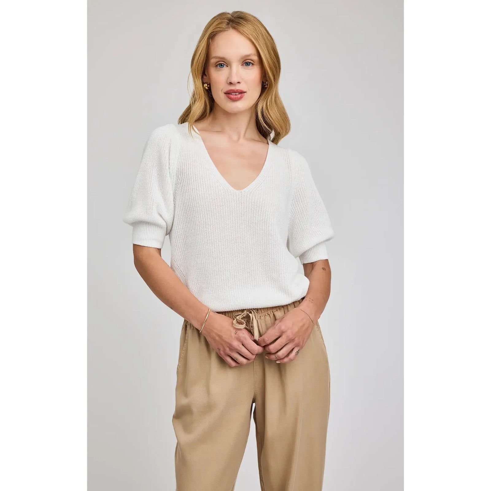 Gentle Fawn Phoebe V-Neck Sweater worn by a woman in a white knit with puff sleeves and tan pants.