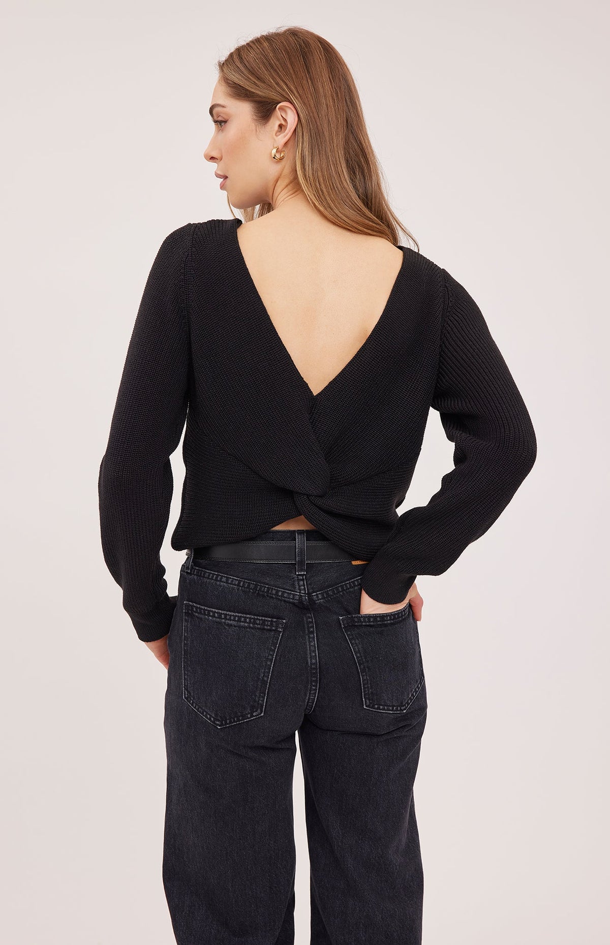 Back view of black Ramona sweater featuring a deep V-opening and twisted detail at the hem, paired with dark denim jeans.