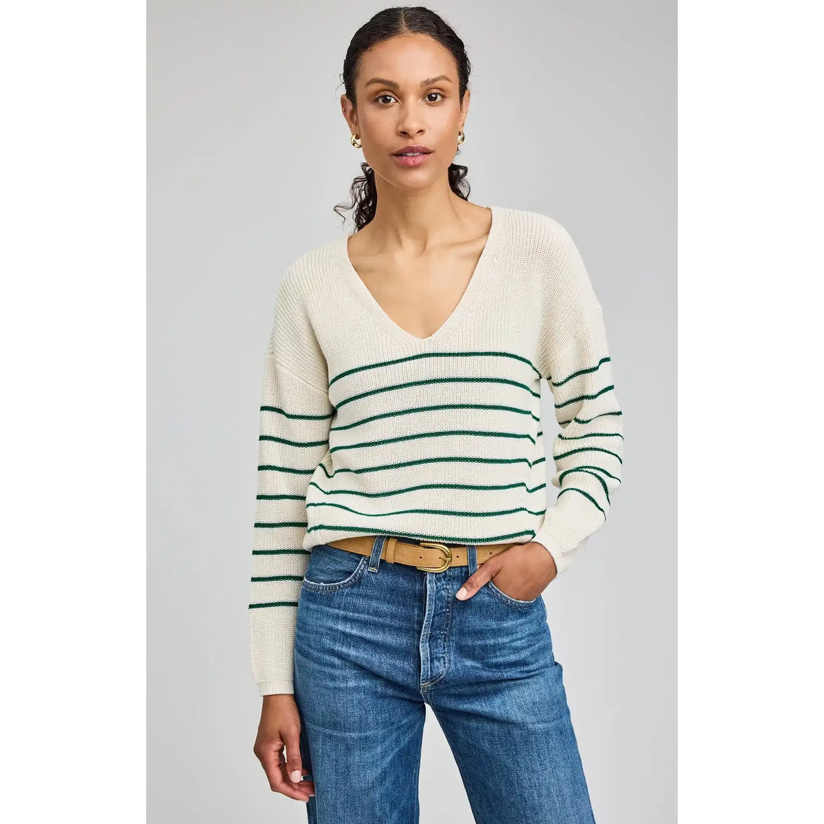Model wears cream Tucker pullover with green stripes, V-neck, relaxed fit, paired with jeans.