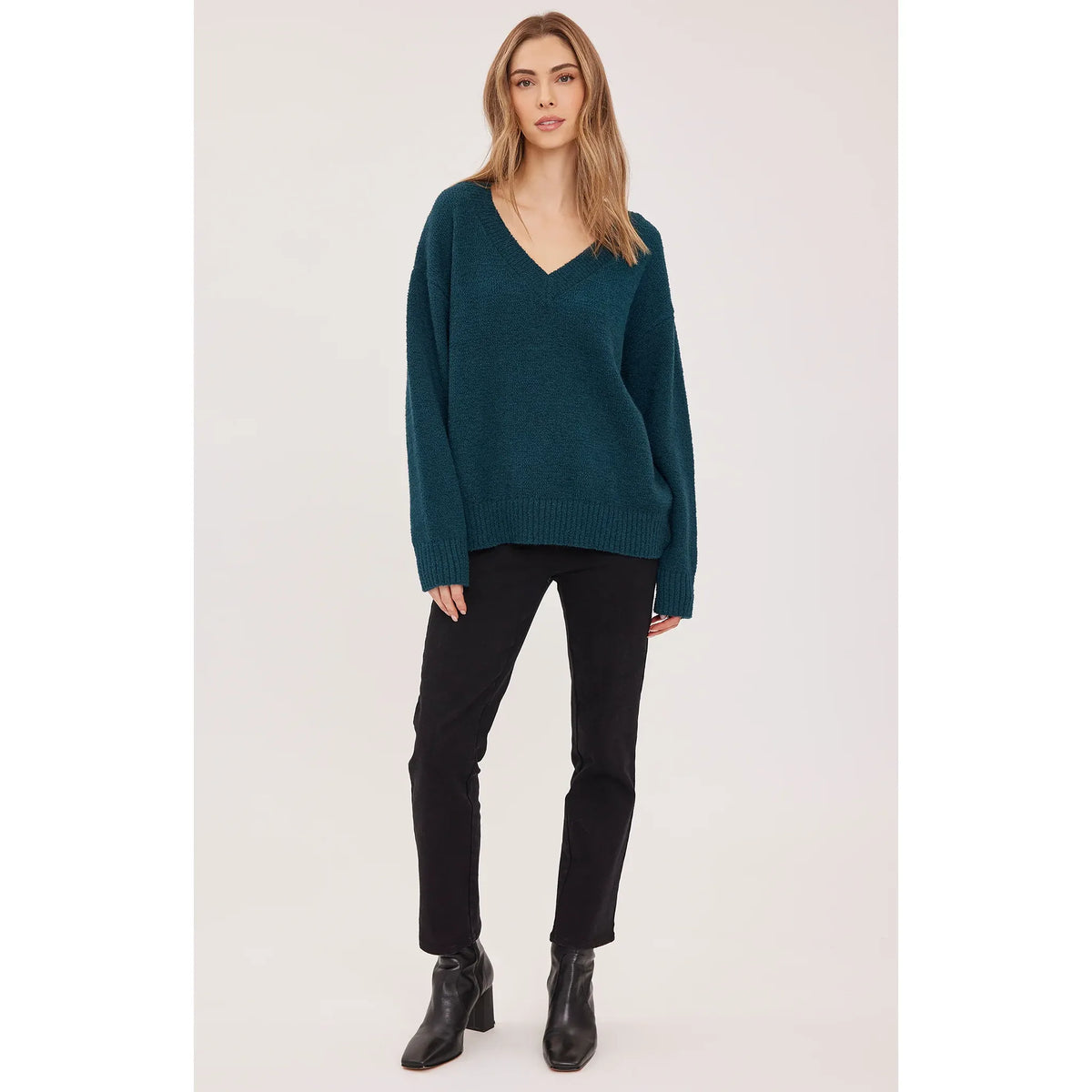 Teal oversized v-neck sweater with soft bouclé texture, ribbed cuffs and hem, styled with black pants and ankle boots.