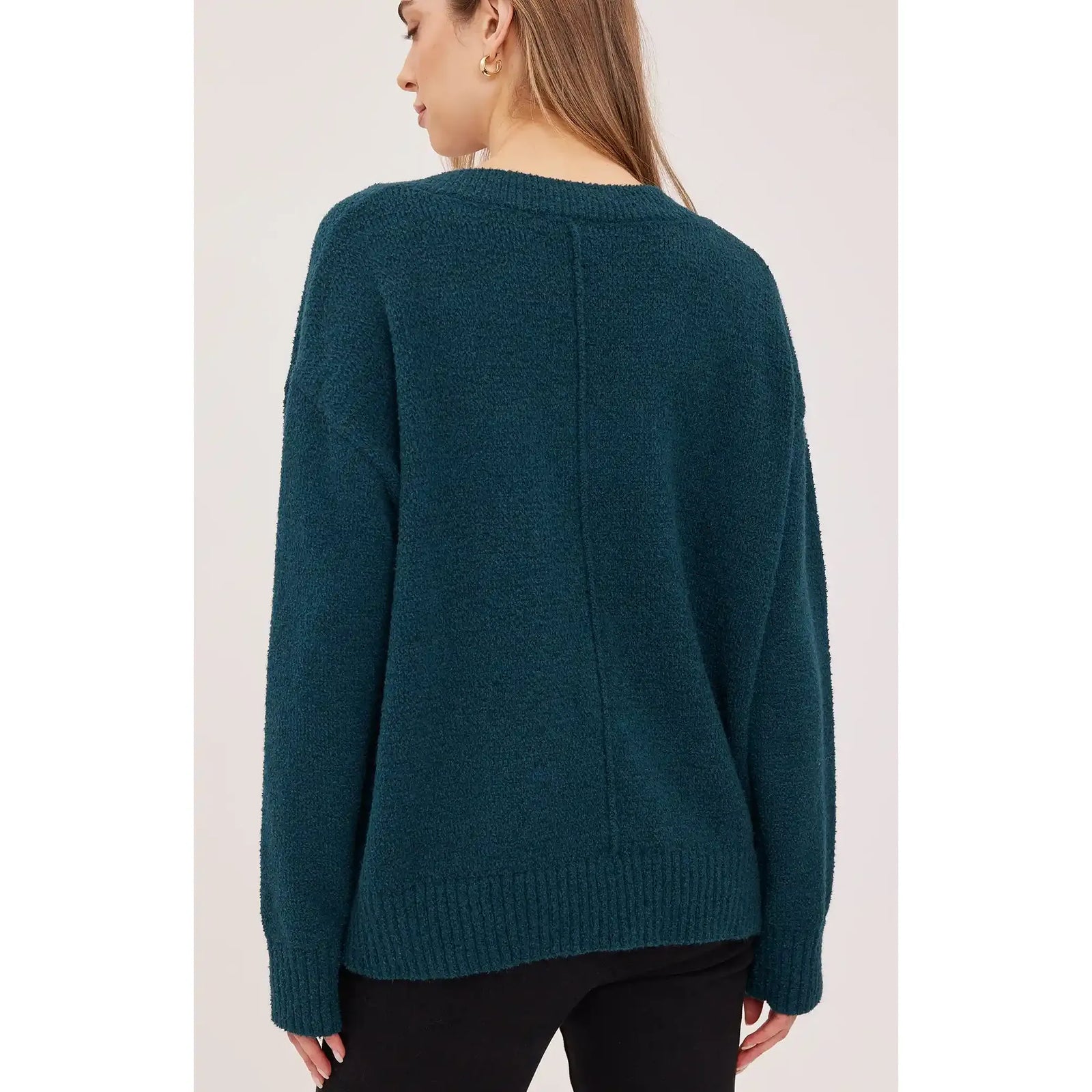 Back view of a dark teal oversized bouclé sweater featuring a ribbed hem, textured knit fabric, and relaxed fit.