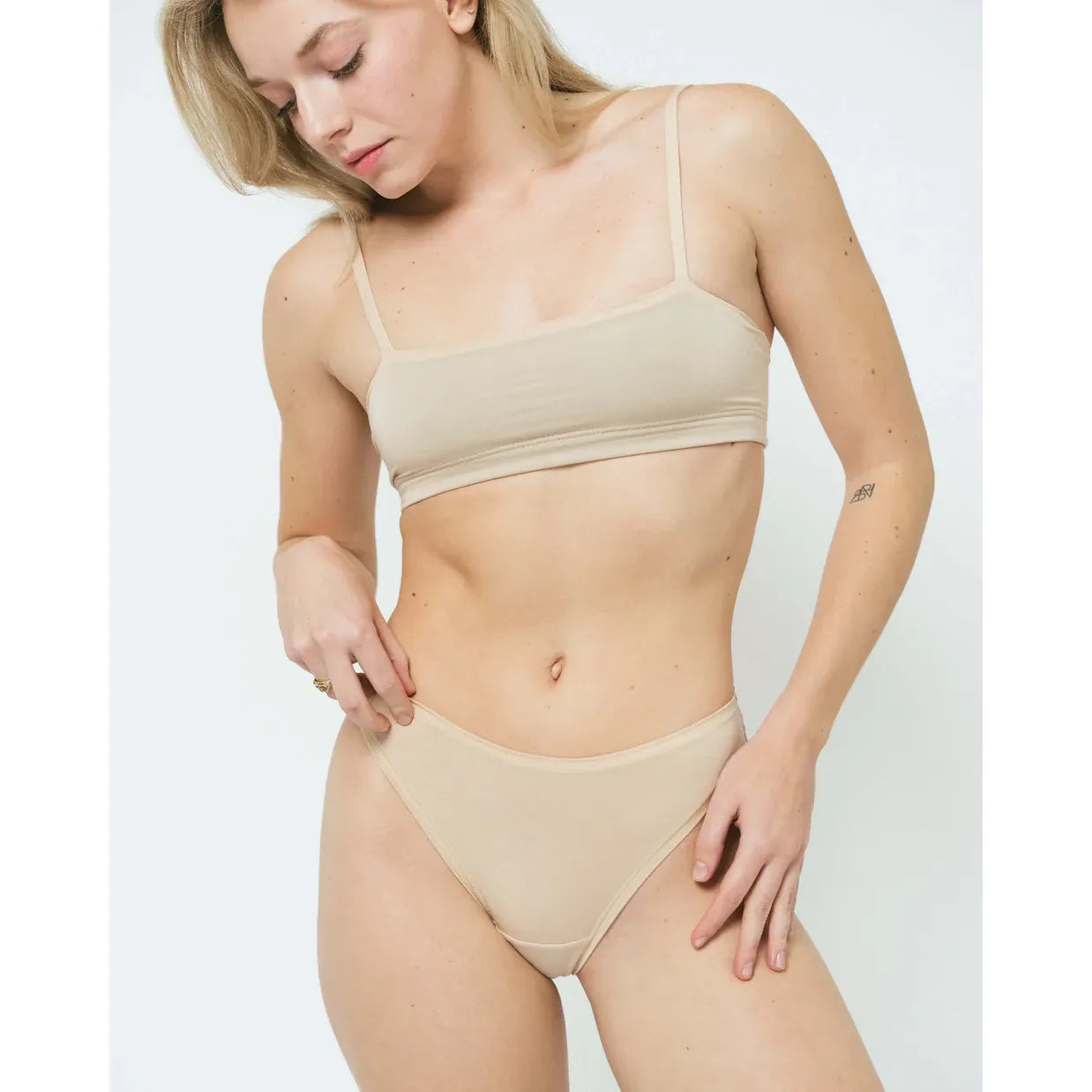 Huha Tata Mineral Bralette in beige; soft, hardware-free bandeau; woman lounging, holding an orange with leaves.