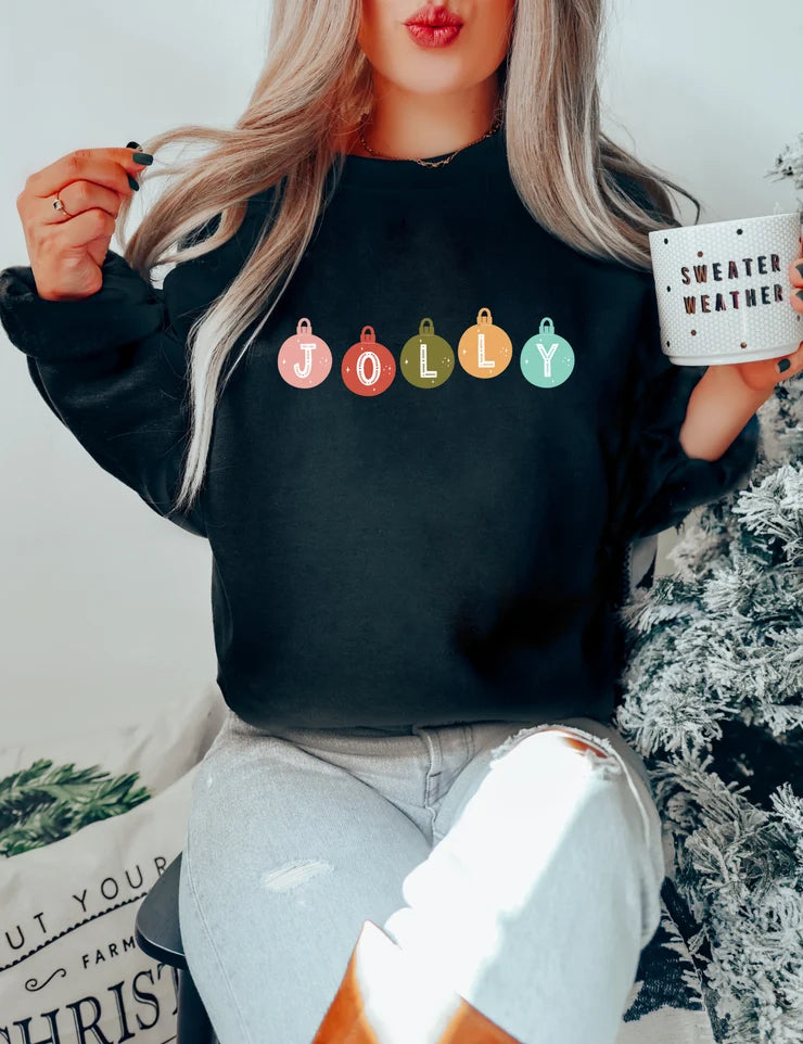 Black crewneck featuring five vintage-style ornaments in pink, red, olive, mustard, and teal that spell "JOLLY" across the chest.