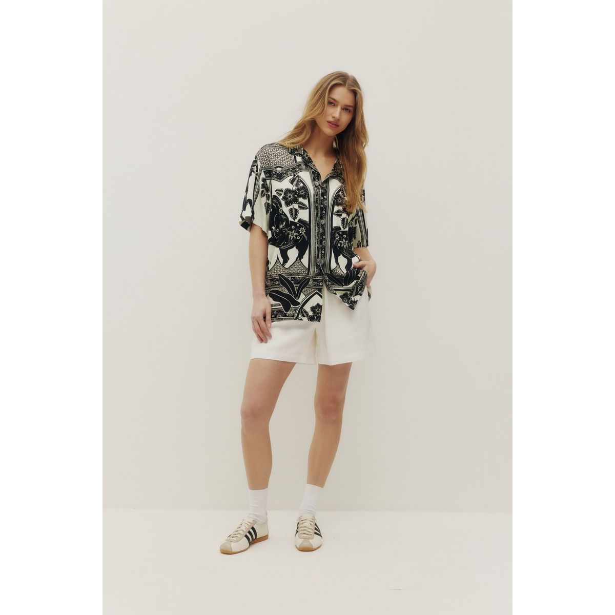 Model wearing Kuwalla Beach Shirt Western Boho with a bold black-and-white print and white shorts.