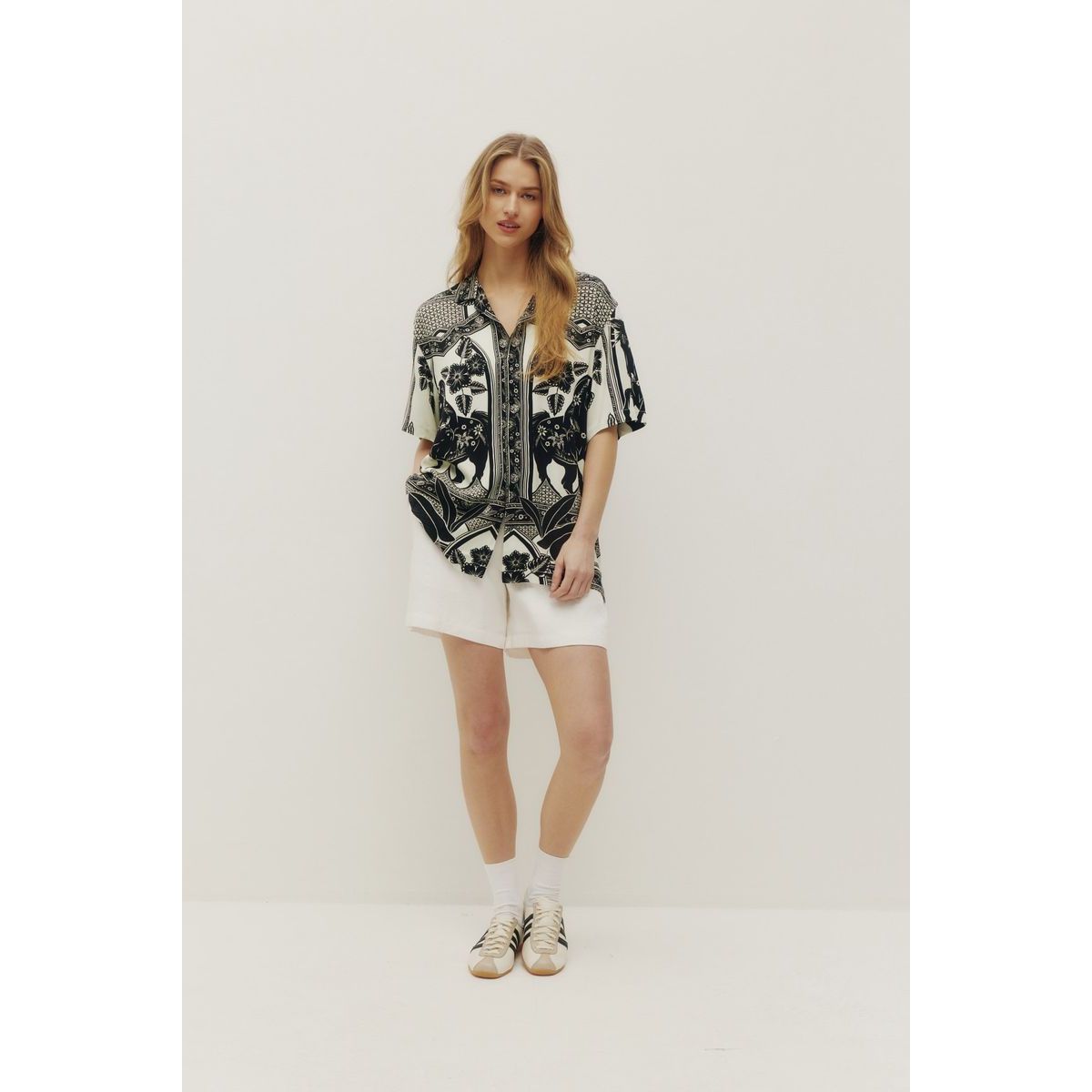Kuwalla Beach Shirt Western Boho in black-and-white palm pattern worn by a model with white shorts.