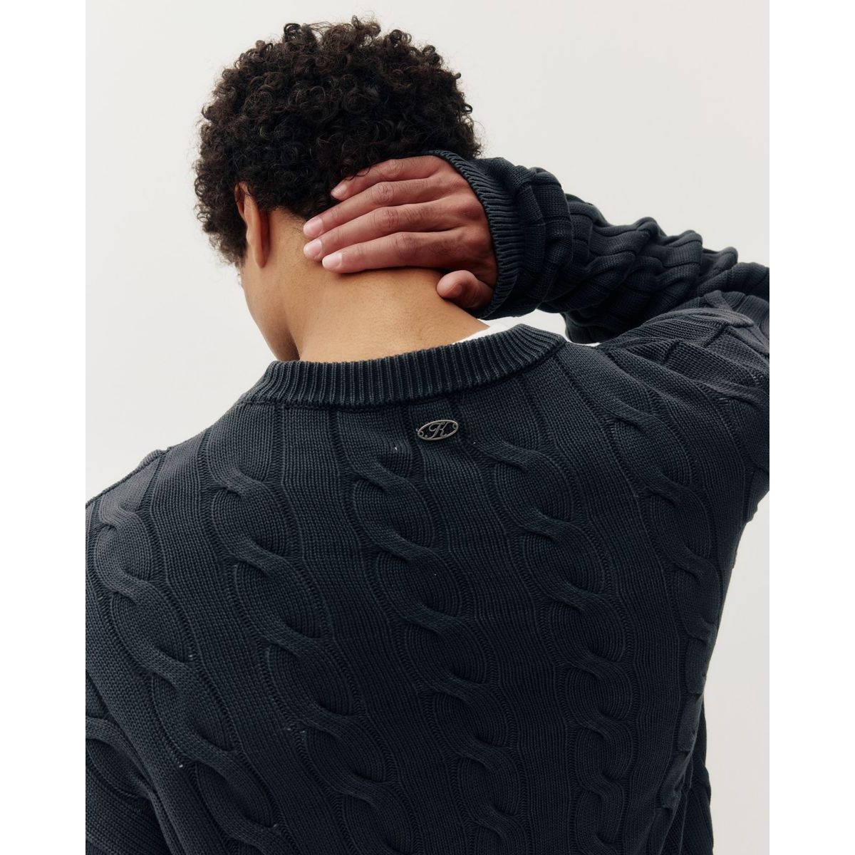 Man wearing a black braided knit box crew sweater and grey pinstripe pants, shown in profile against a white background.