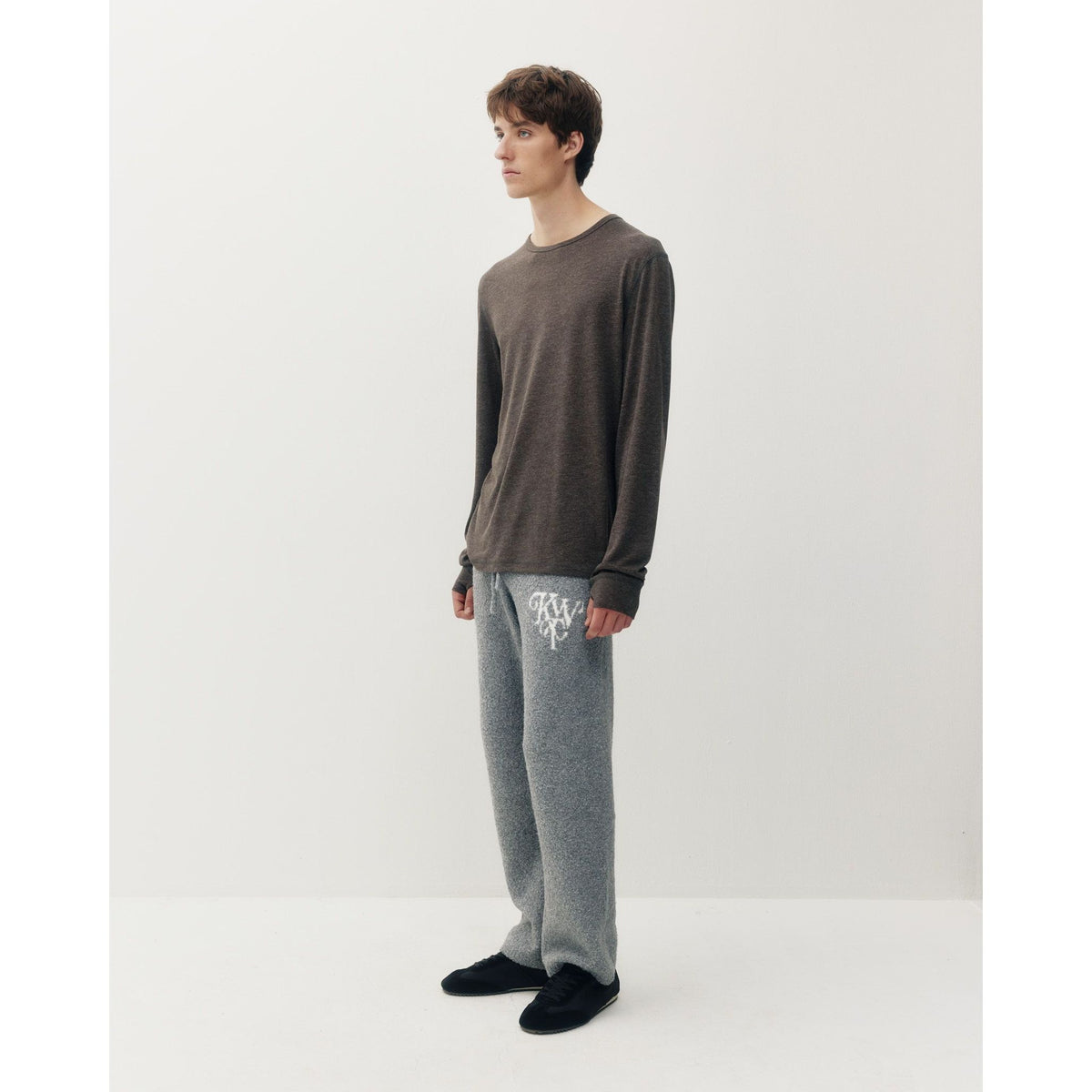 Man modeling dark brown heathered thermal long sleeve tee with soft texture, paired with grey logo sweatpants and black sneakers against white background.