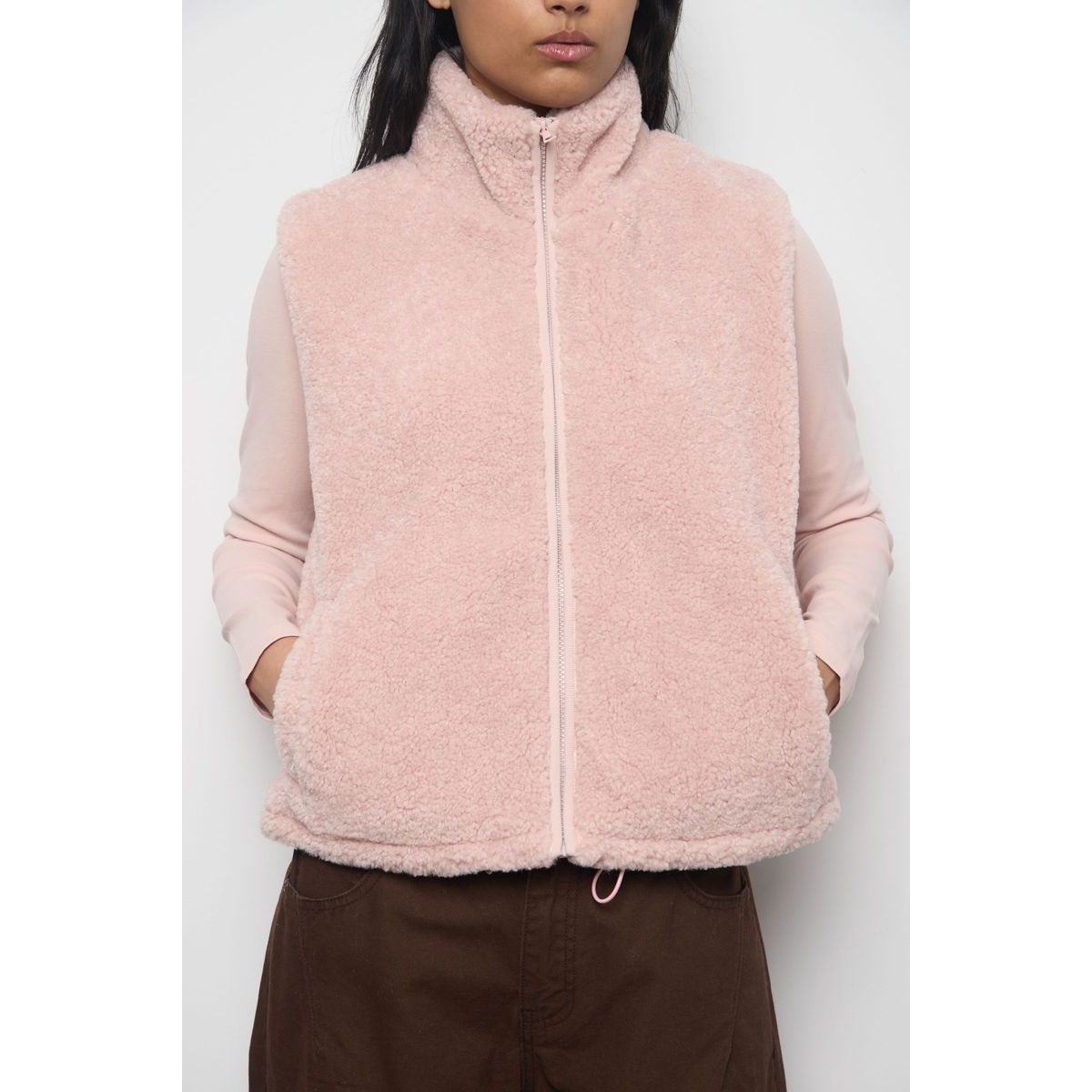 Light pink faux fur zip-up vest with high collar and drawstring hem, styled over a matching long-sleeve top for cozy transitional wear.