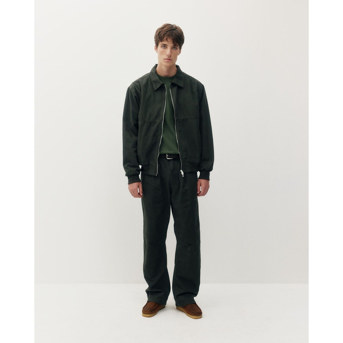 Man wearing dark green Oxford Bomber jacket with structured collar and zip front, paired with matching utility pants and brown loafers.