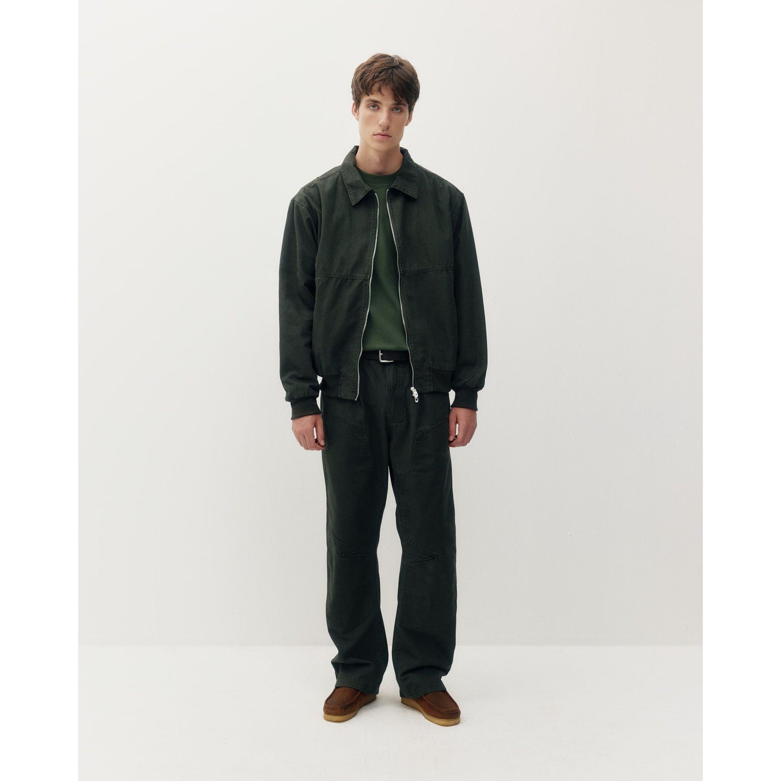 Man wearing dark green Oxford Bomber jacket with structured collar and zip front, paired with matching utility pants and brown loafers.