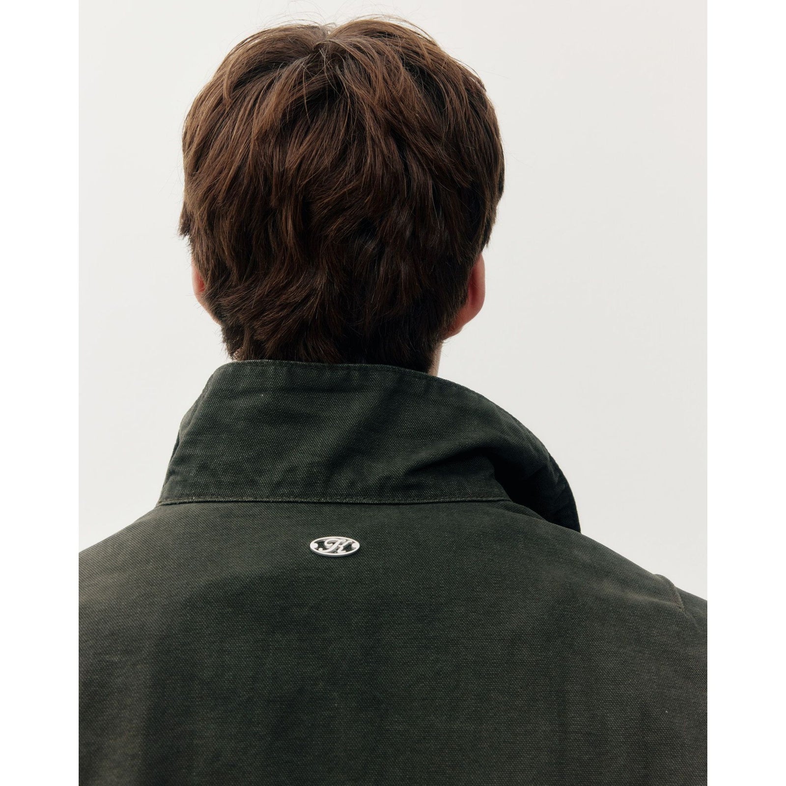Back view of a dark green cotton Oxford Bomber jacket featuring a structured collar and silver K logo emblem on the neck.