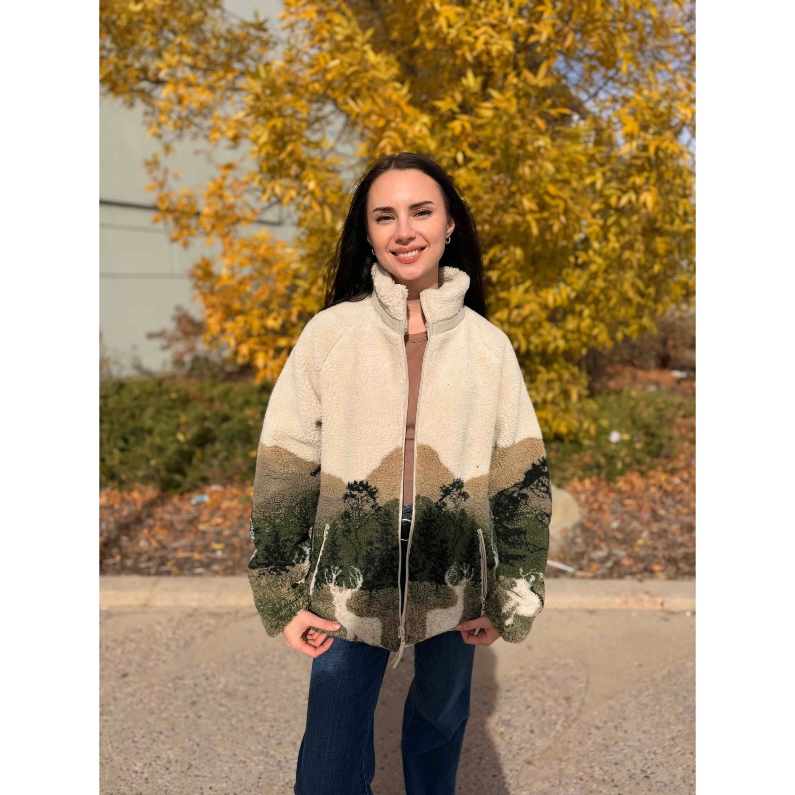 Beige sherpa jacket featuring an elk wildlife and forest print across the lower half, with zippered pockets and a full-length zipper for cozy layering.