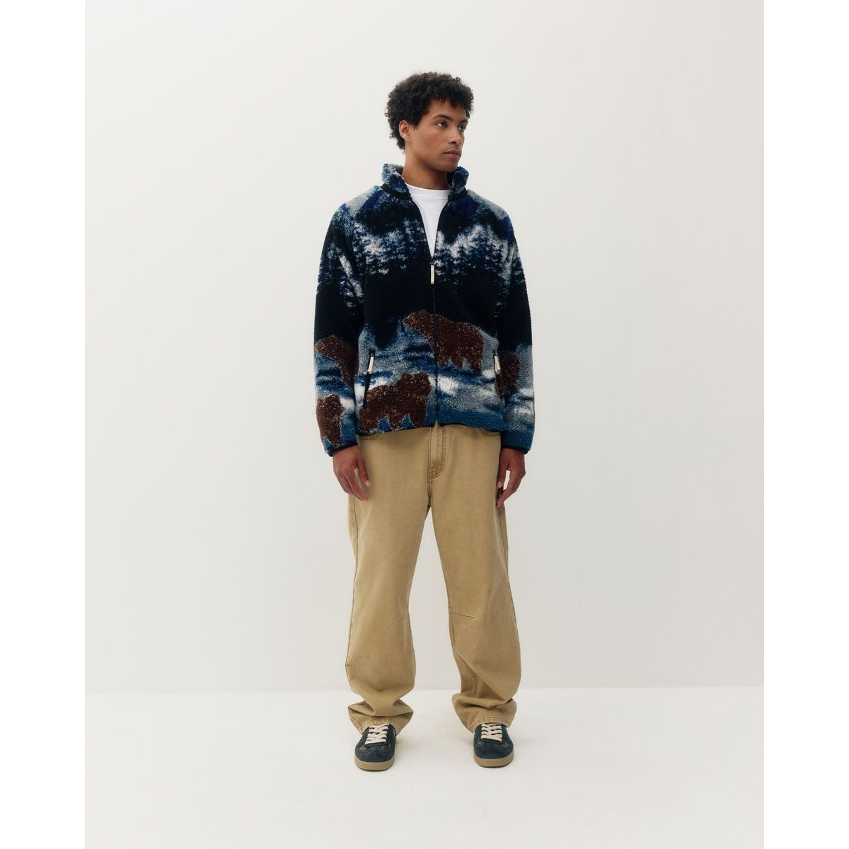 Man wearing a blue printed sherpa fleece jacket featuring a bears in the wild design, paired with beige pants.