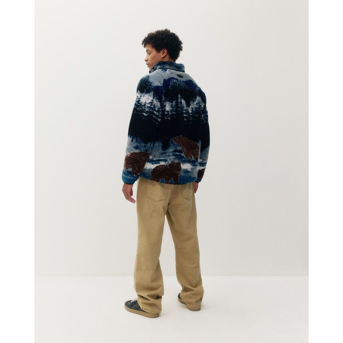 Back view of printed sherpa jacket featuring bears in a forest design, soft terry fleece texture, and relaxed fit with khaki pants.