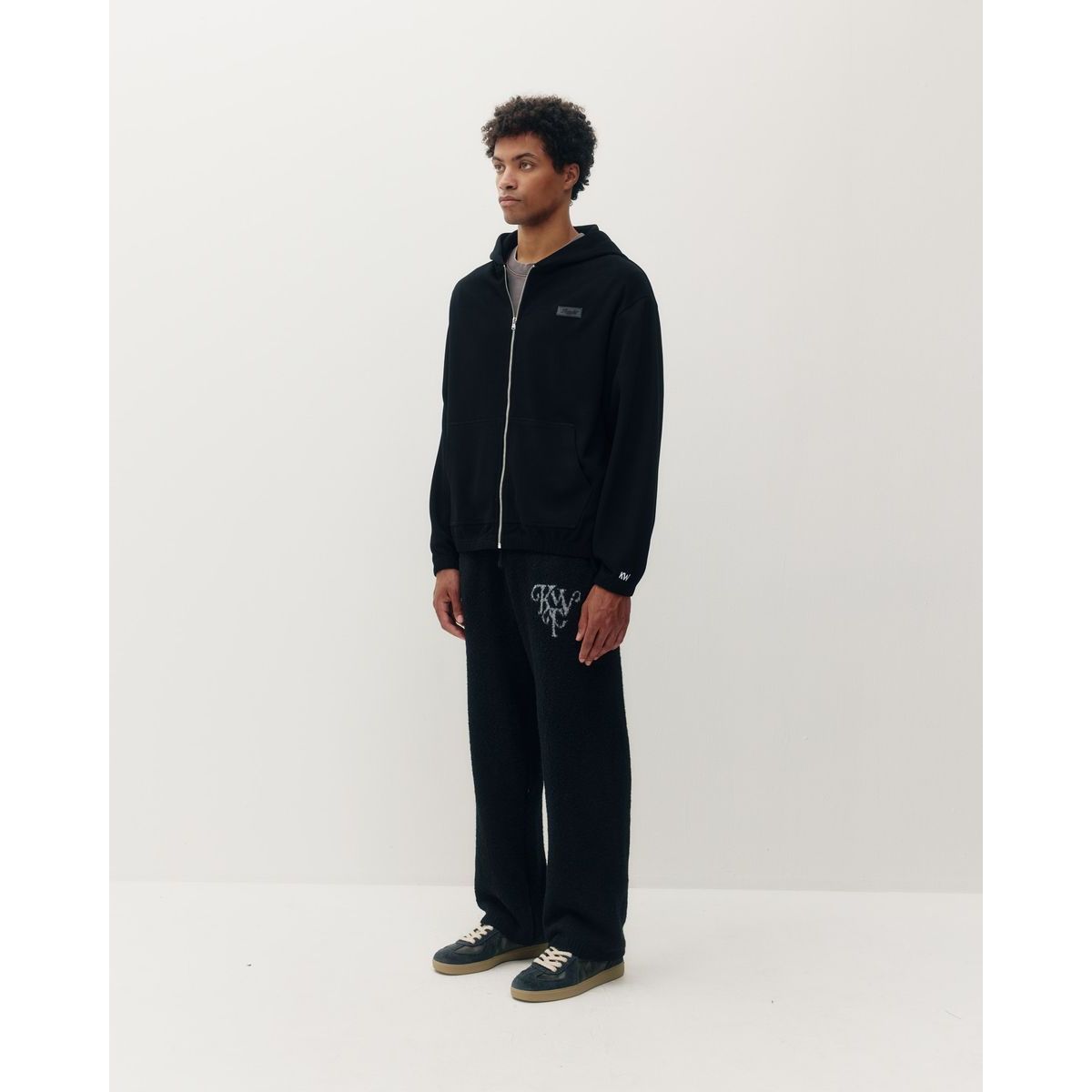 Man wearing black Kuwalla ribbed zip hoodie with silver zipper and matching textured sweatpants featuring embroidered logo.