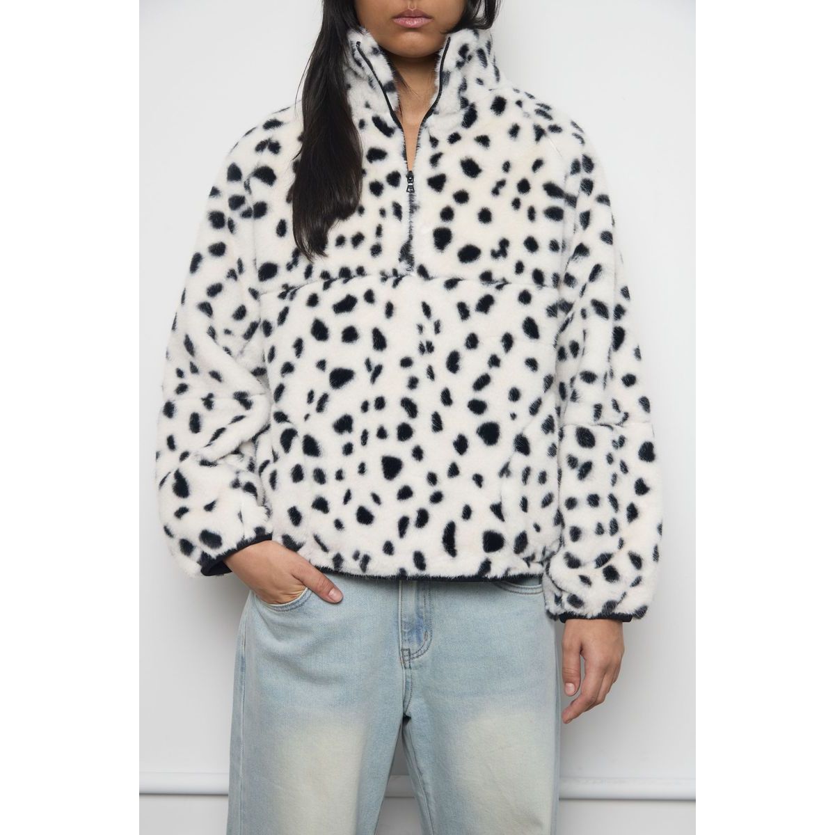 White faux fur jacket with black spots, half-zip collar, and plush texture paired with light blue jeans.
