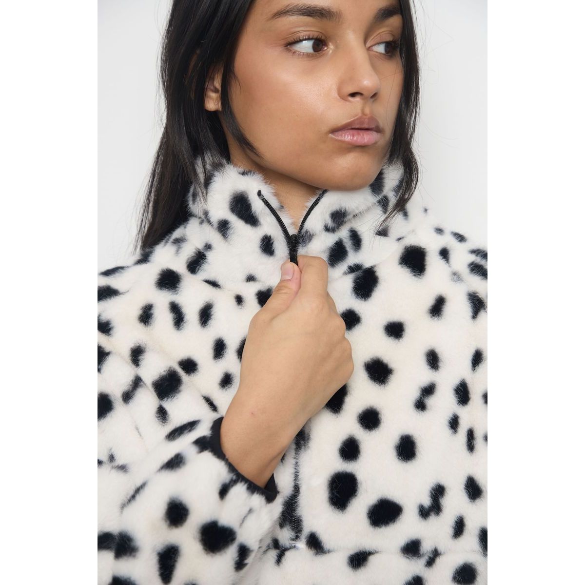 Close-up of a plush white faux fur jacket with black spots and a high zip collar, showcasing soft texture and modern streetwear style.
