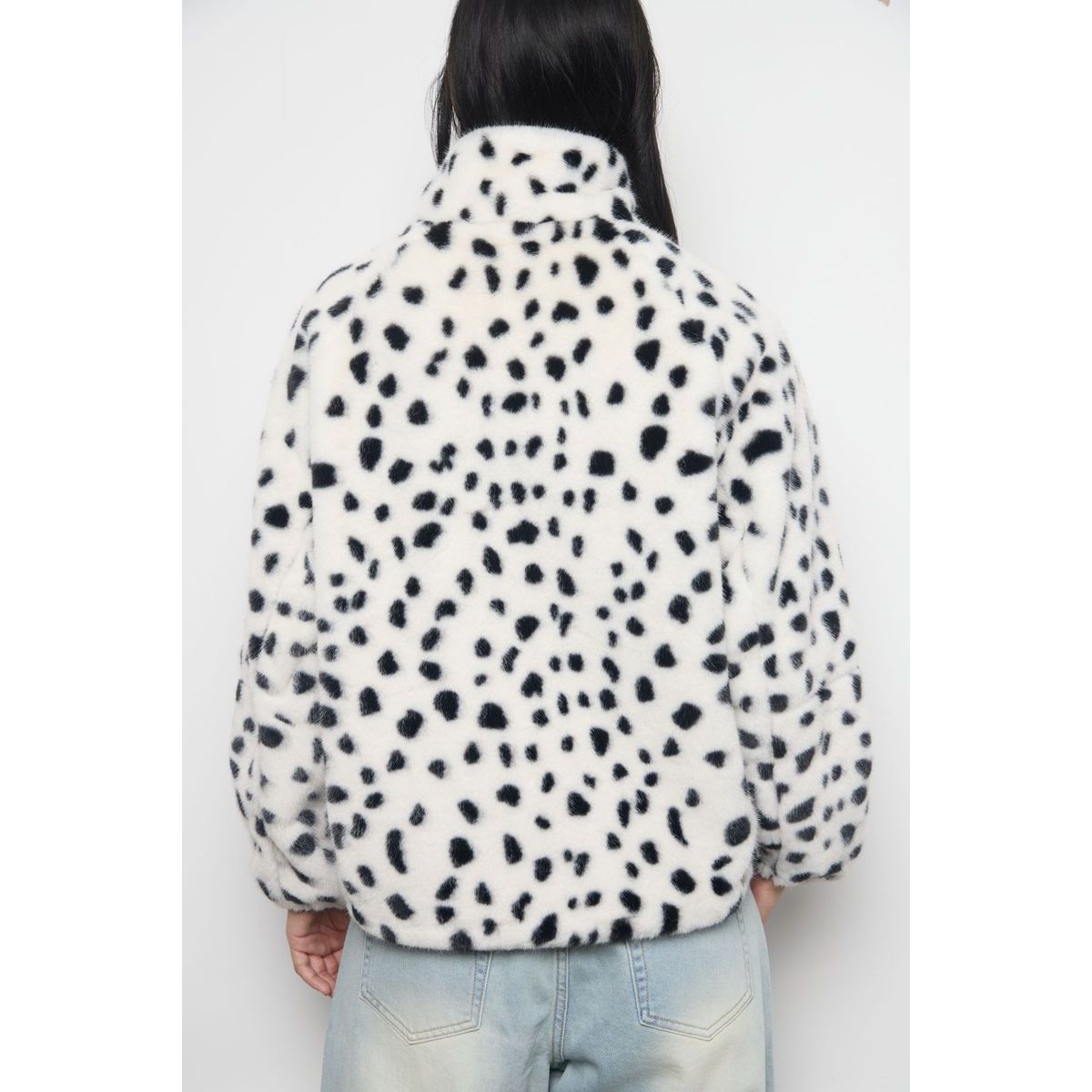 Back view of white faux fur zip-up jacket with black dalmatian spots, featuring plush texture and high collar streetwear design.