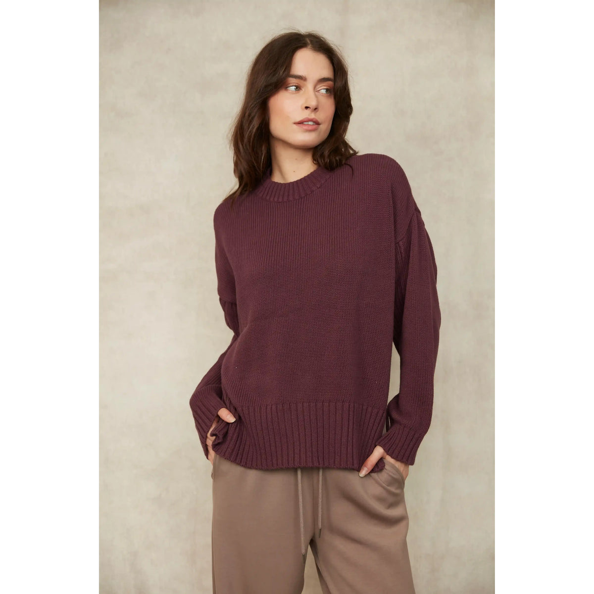 Woman wearing a burgundy long sleeve crew neck cotton knit pullover with ribbed trim at the hem and cuffs.