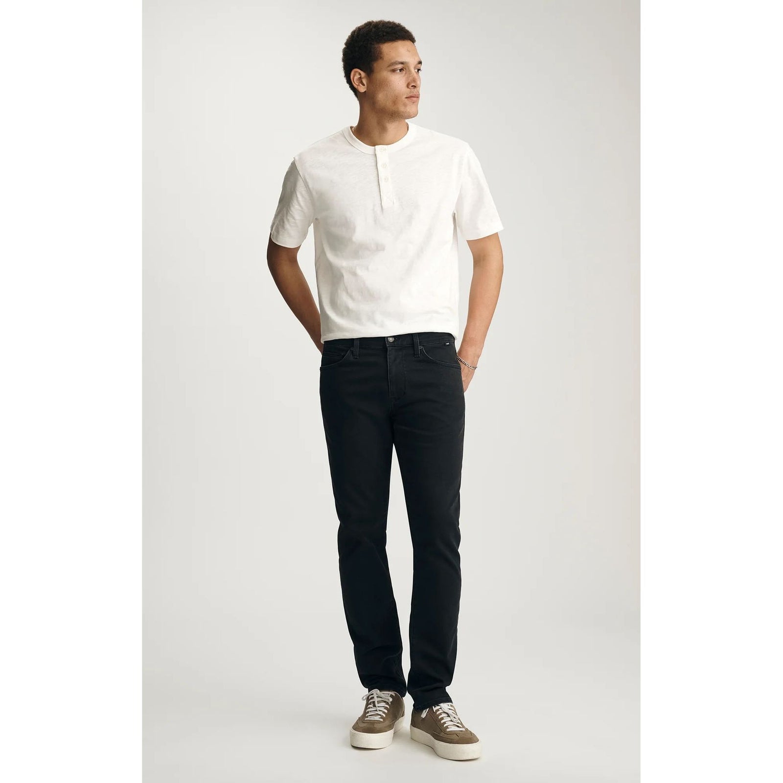 Mavi Jake Smoke Explorer Denim in washed-out black, slim-fit jeans on a man in a white tee and tan sneakers.