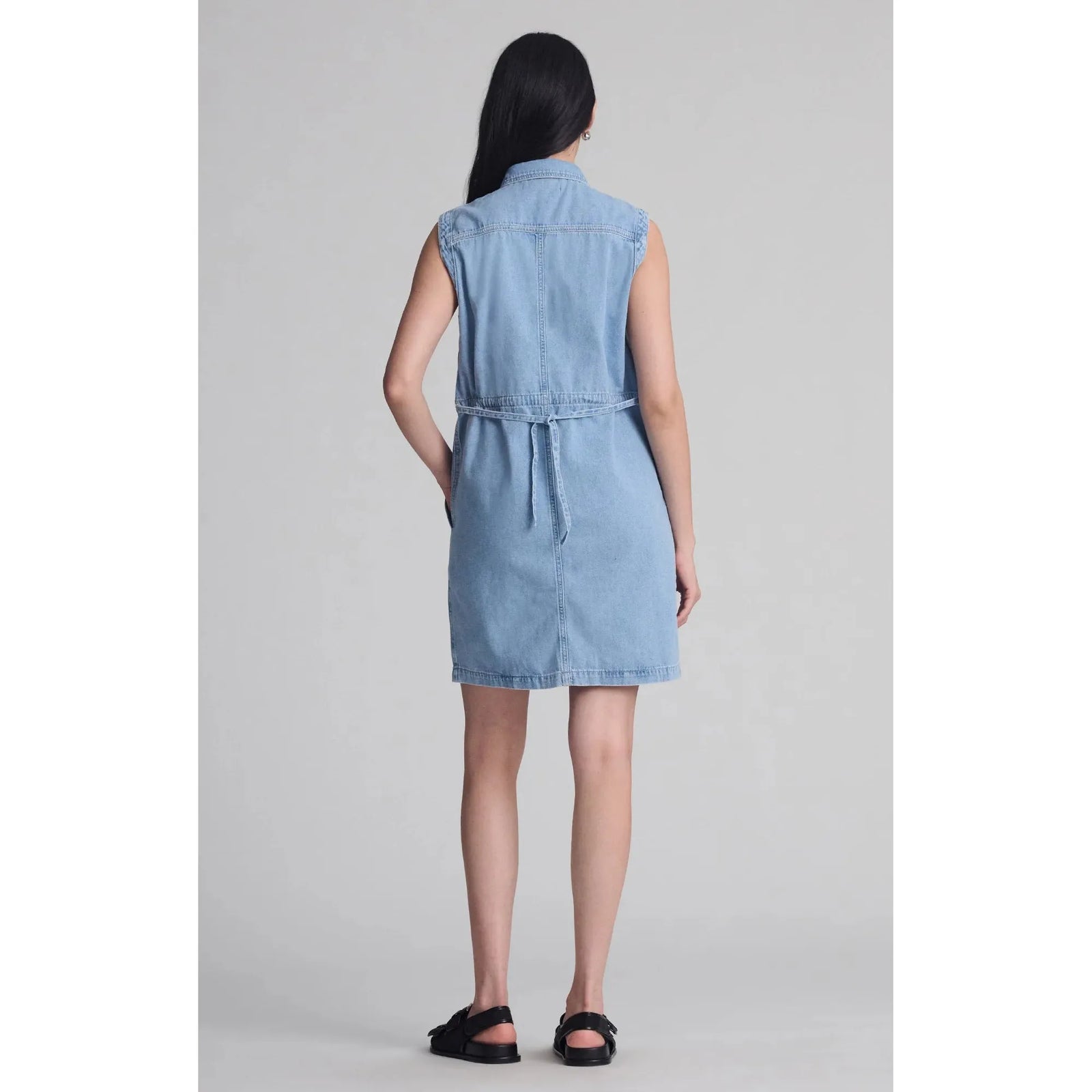Woman wearing a sleeveless denim Mavi Simla Pocket Dress with back tie detail and black sandals from Mavi.