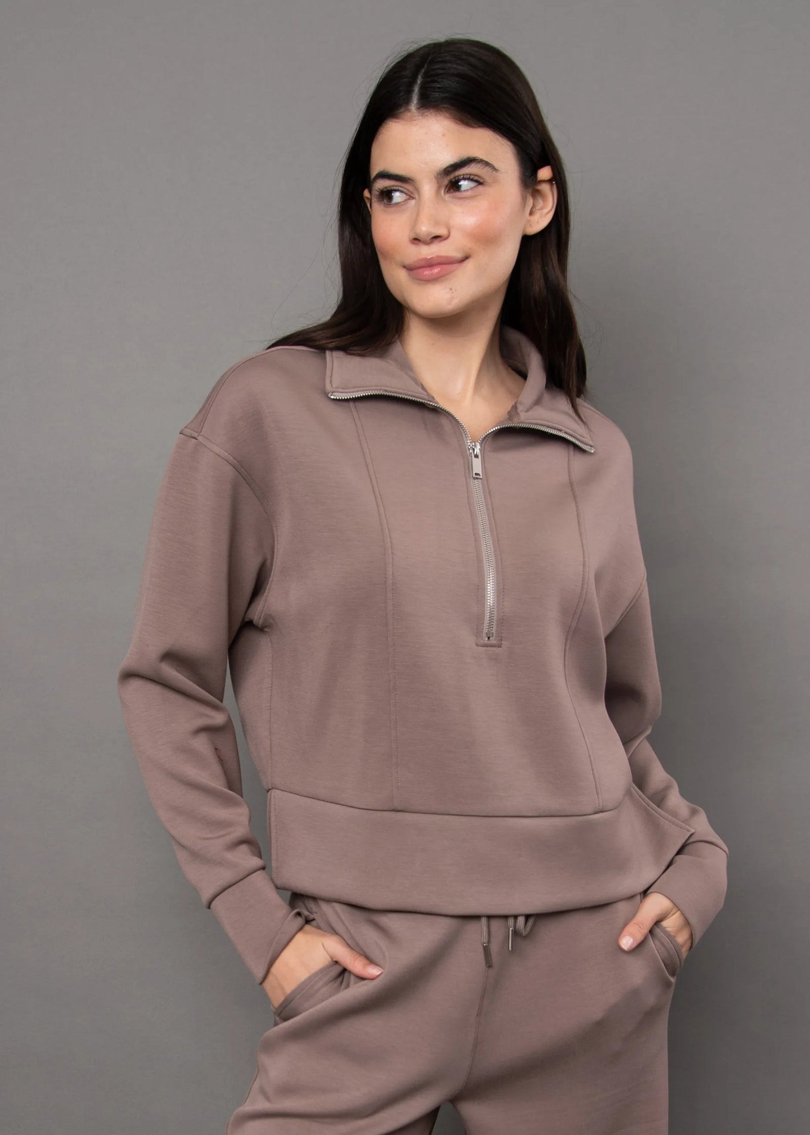 Woman wearing a dusty rose soft knit zip-up top with a quarter-zip collar and relaxed fit, paired with matching pants.